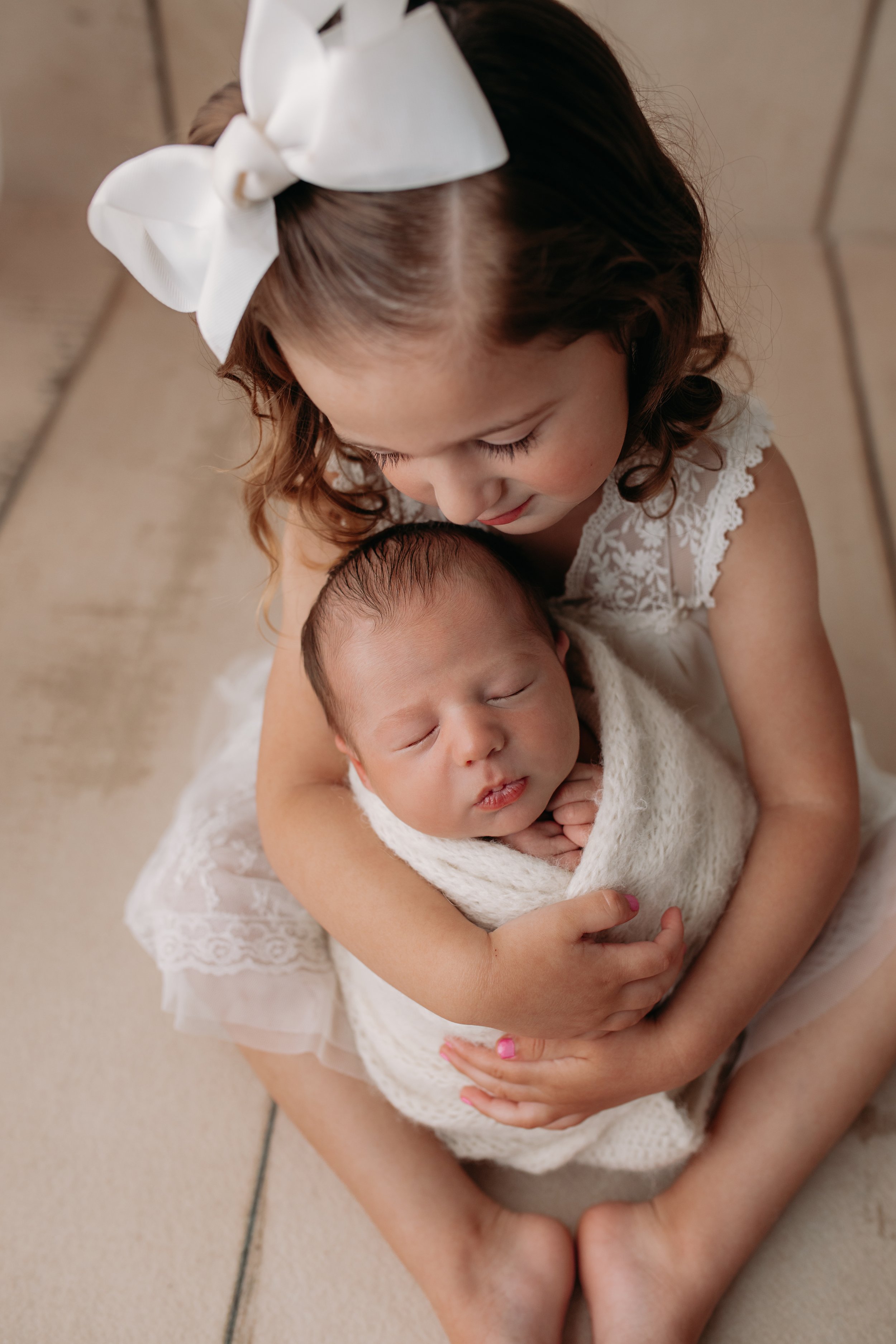 Big sister holding newborn baby brother while gazing with love during Newborn Session with Chasing Sammi Photography in Springfield Missouri