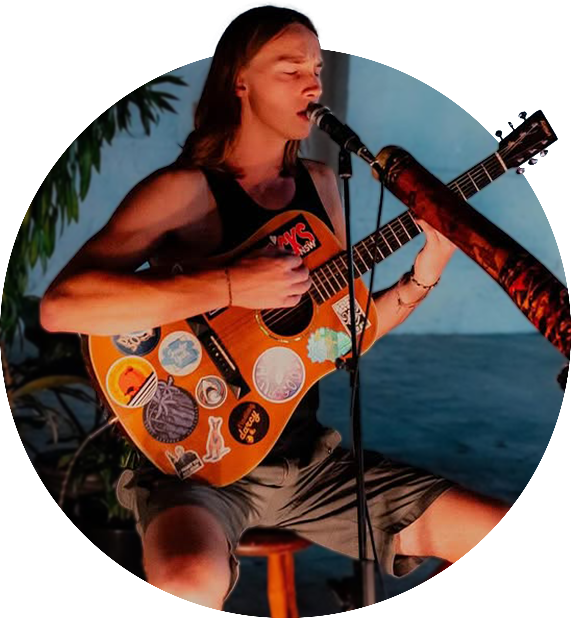 A young man with shoulder-length hair, singing at PASS PAUSE PLAY at Nauti Studios Sydney.