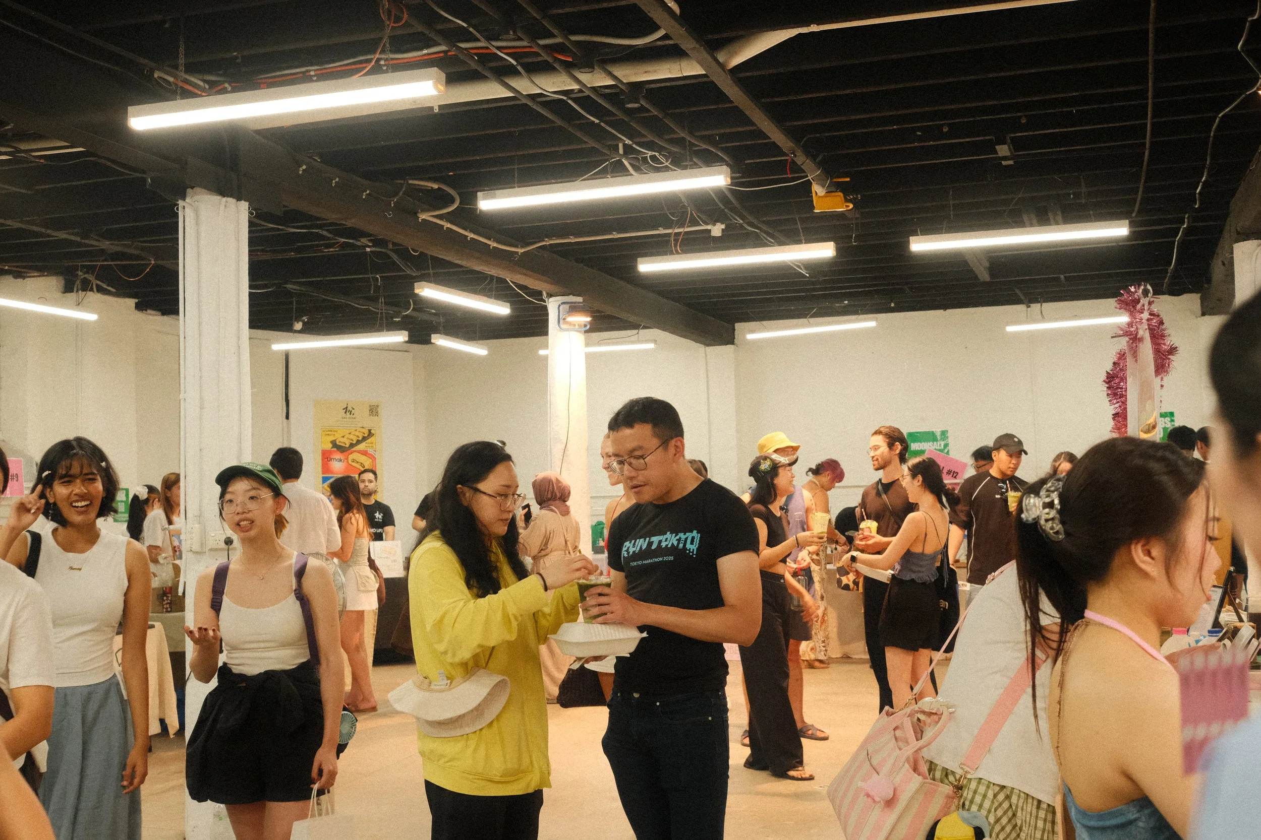 People gathered at an indoor market event, some eating and chatting at Nauti Studios Sydney.