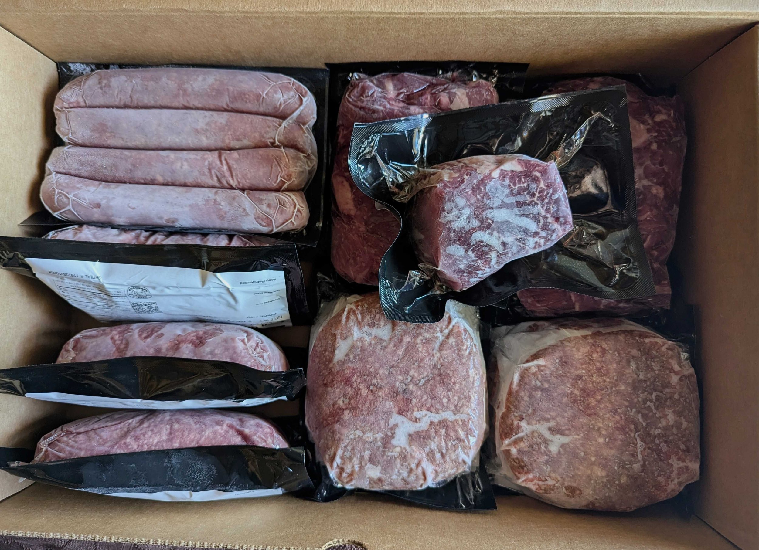 Top down view of a box of frozen beef cuts: steak, burgers, sausages