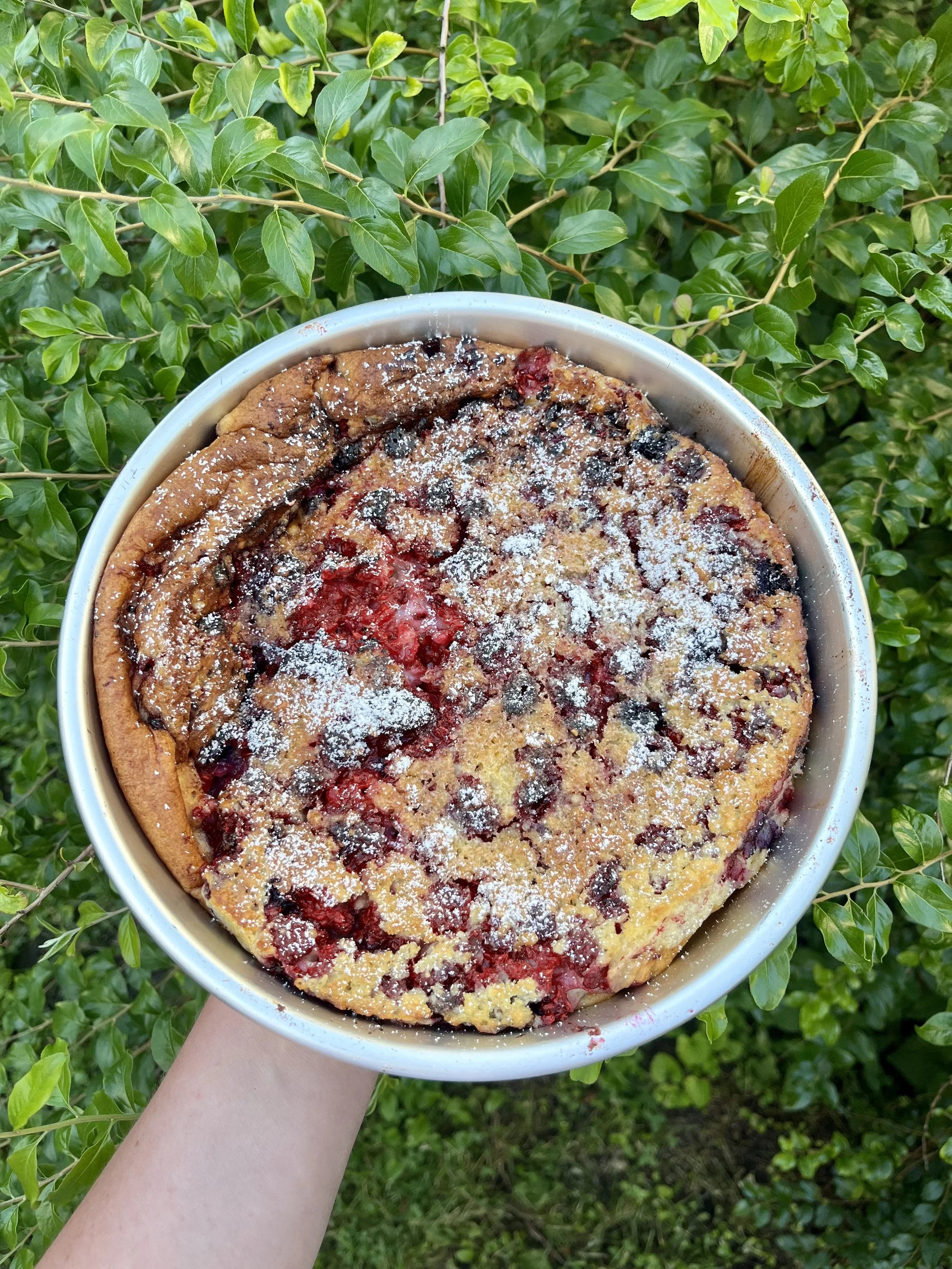 Berry-filled dessert being held out over top of a lush green background