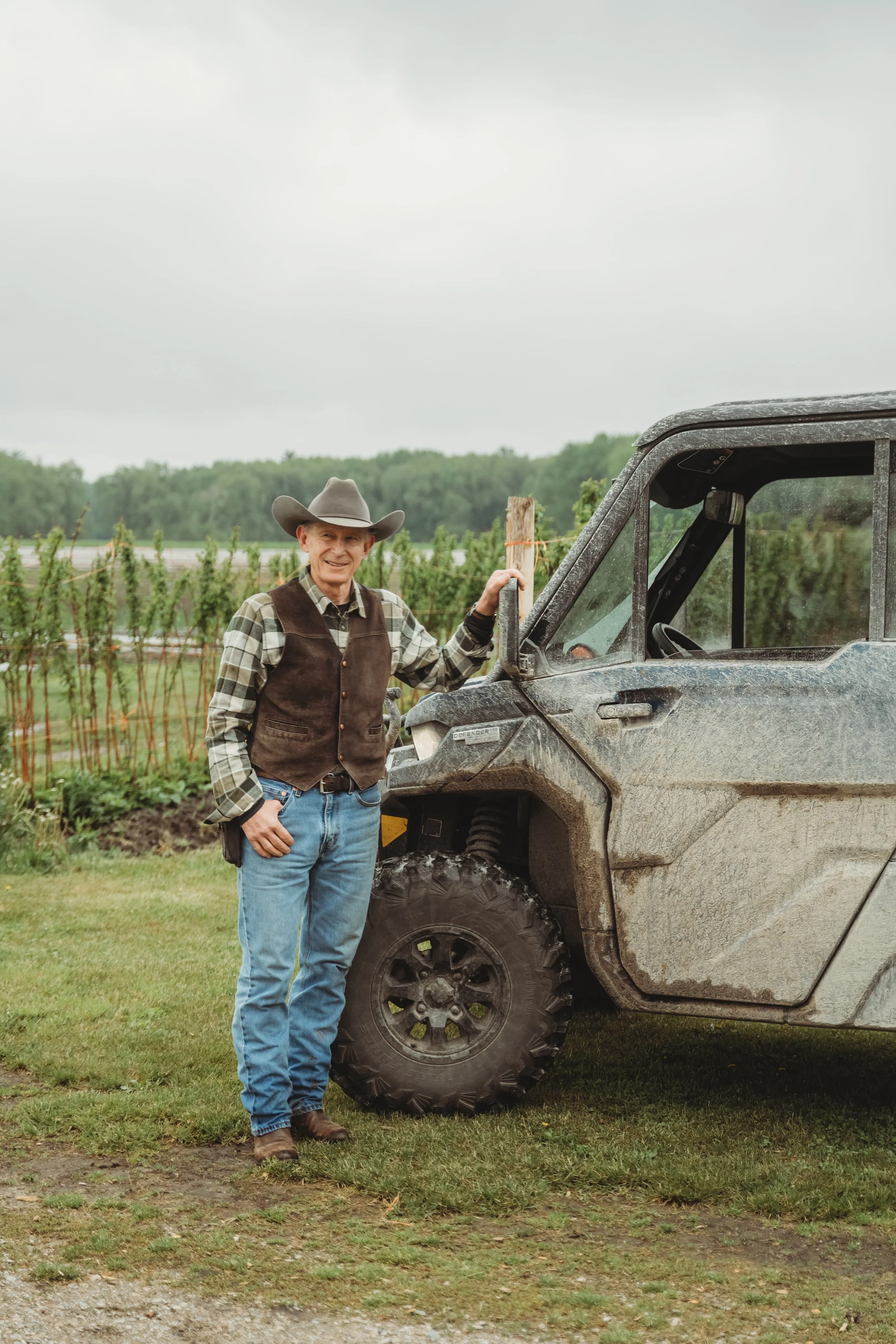 Man wearing a cowboy hat, vest, and boots leaning on a Can Am vehicle