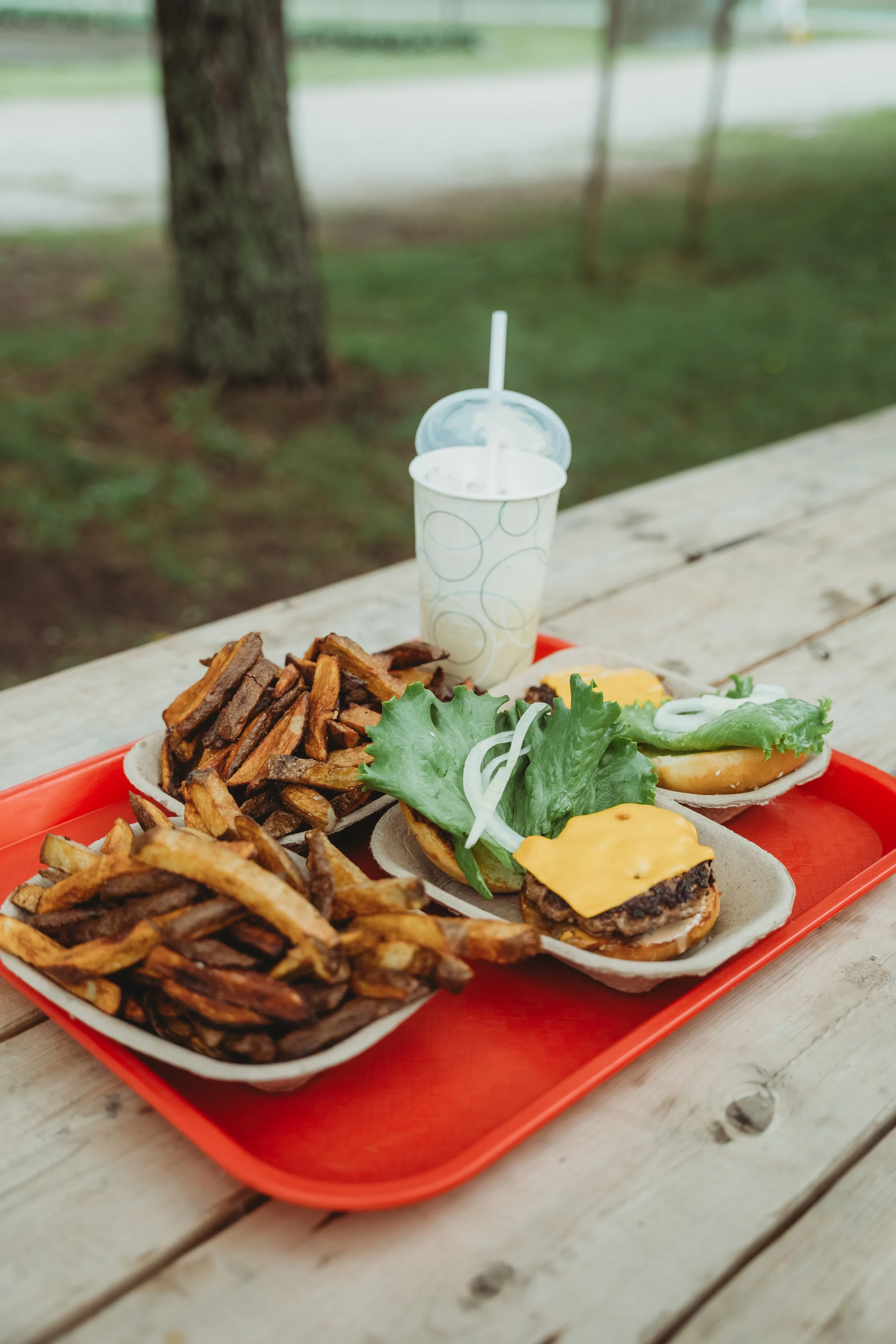 A red tray full of burgers, fries, and a milkshake