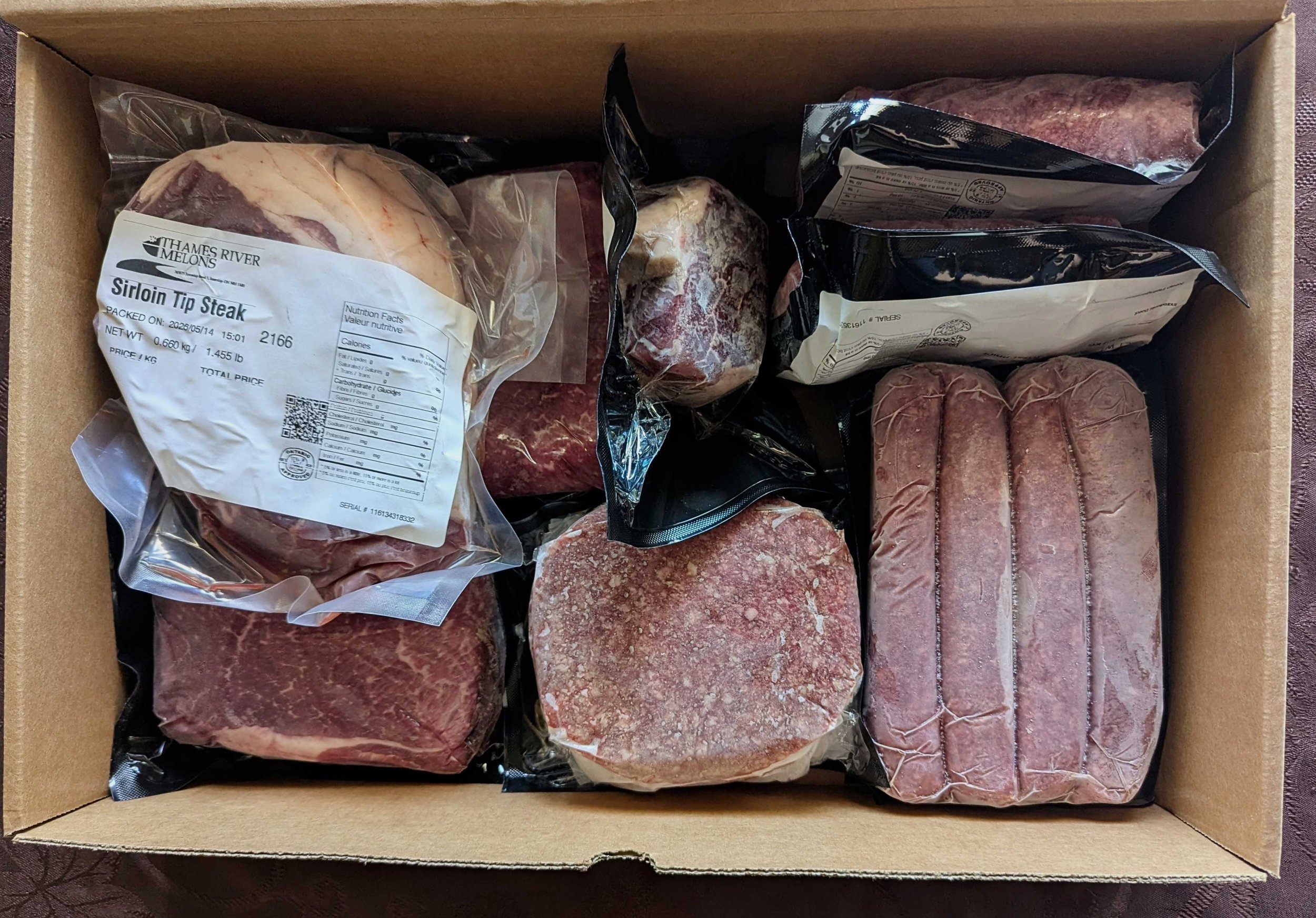 Top down view of a box of frozen beef cuts: steak, burgers, sausages