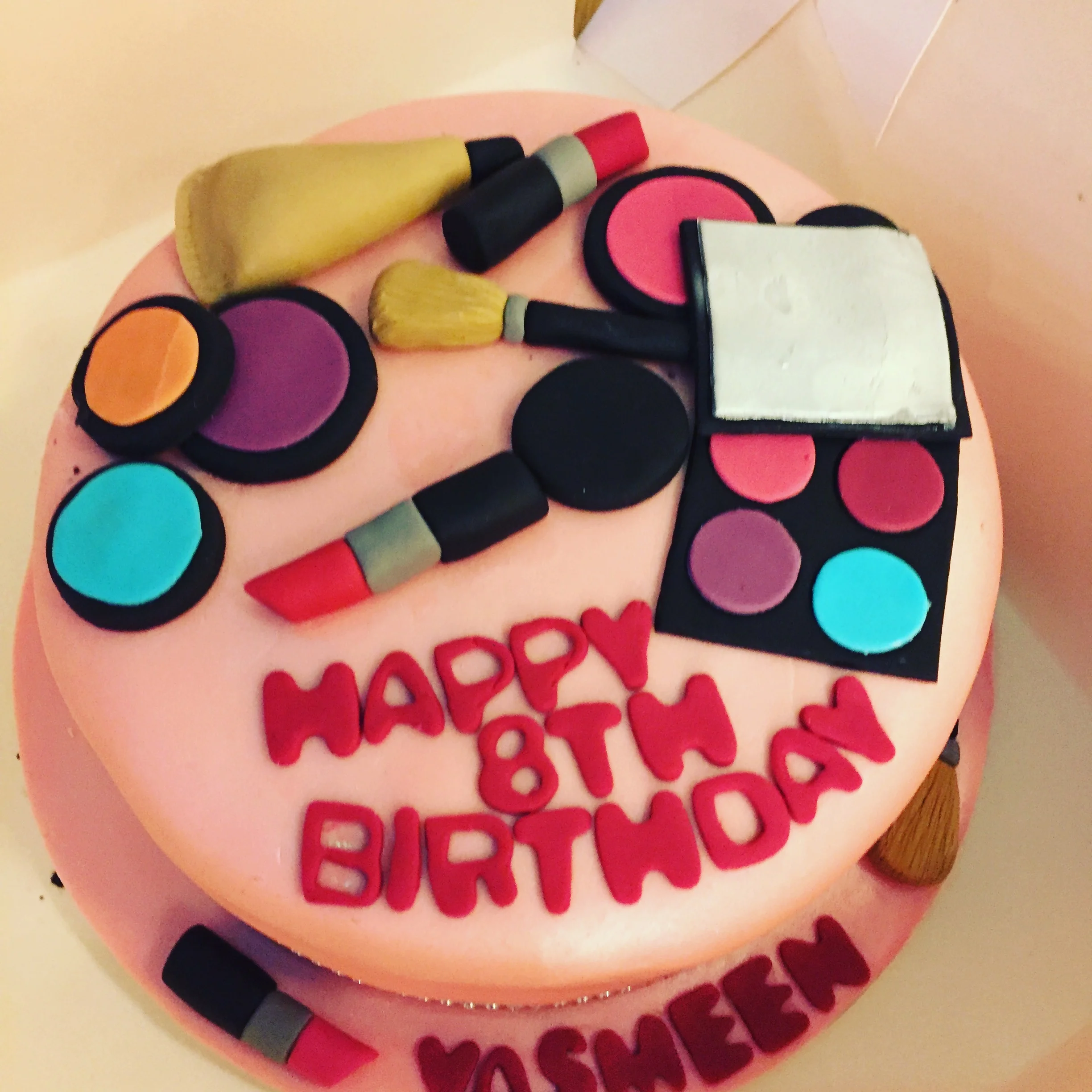 Pink birthday cake with colorful round decorations and red fondant letters that spell out "Happy Birthday."