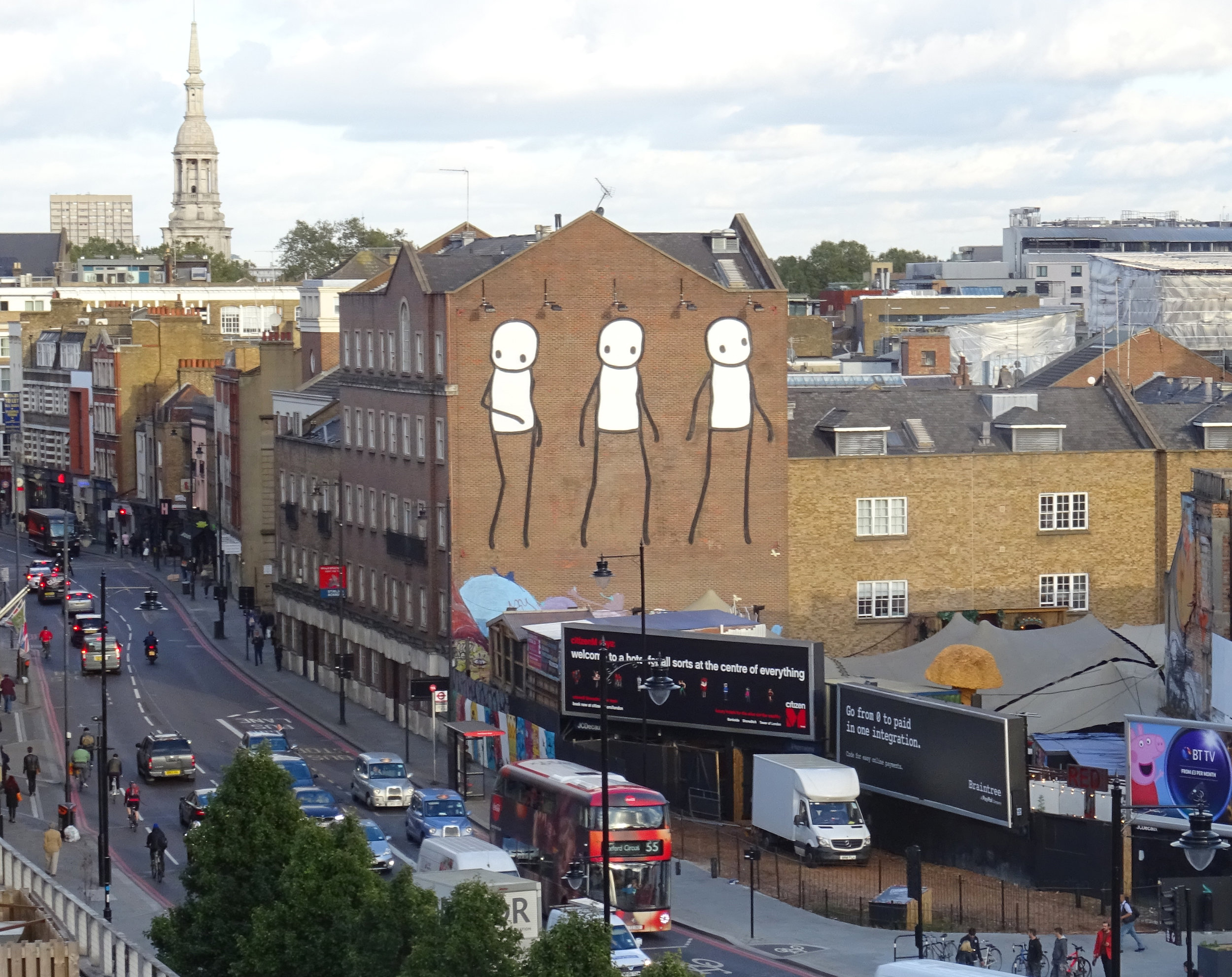 Past, Present and Future Three figures representing the past, present and future of Shoreditch rise high over the former artists’ district, home now to only a handful of artists. The first figure looks longingly back on Old Street where artists once thrived, the second peers out at the encroaching billboards, uncertain of how long the few remaining artists can afford to stay, the third teeters precariously, to succeed or move on is yet to be seen. This mural is intermittently obscured by an advertising hoarding and is visible only on certain weeks of the year. 