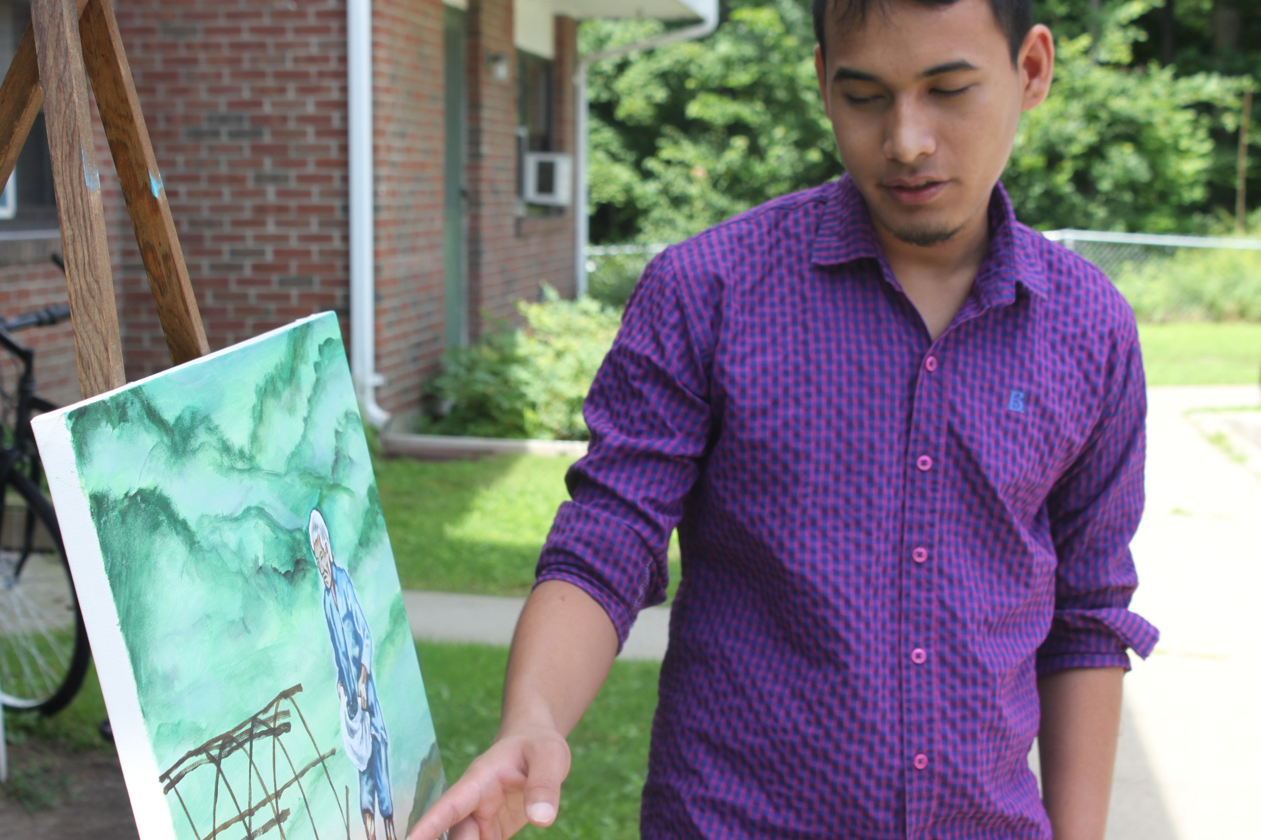 Hom Pradham explains one of his paintings outside his home in Winooski, Vermont.