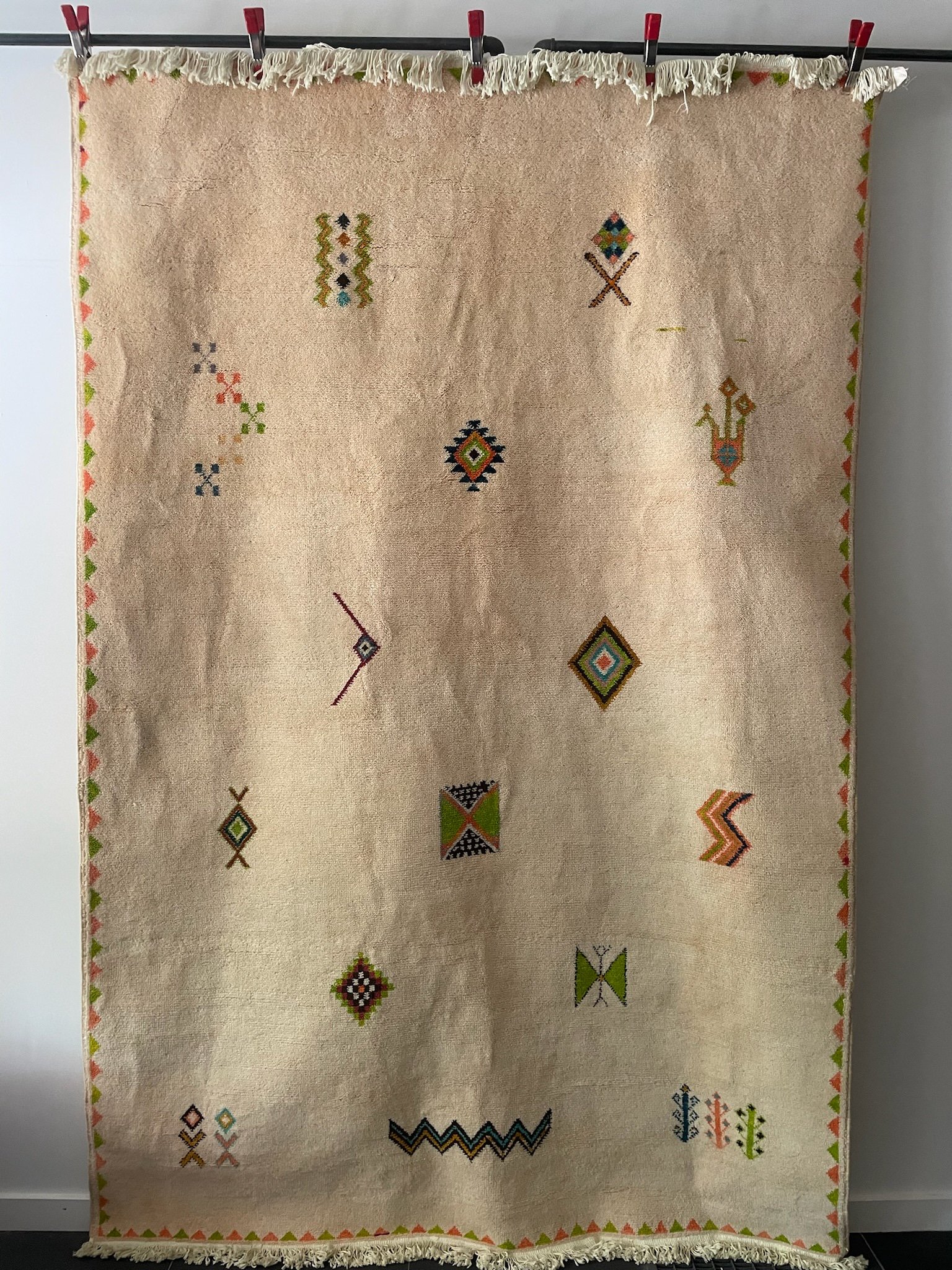 low-pile, hand-knotted, Moroccan wool rug with cream base and minimal pink, green and blue Berber designs