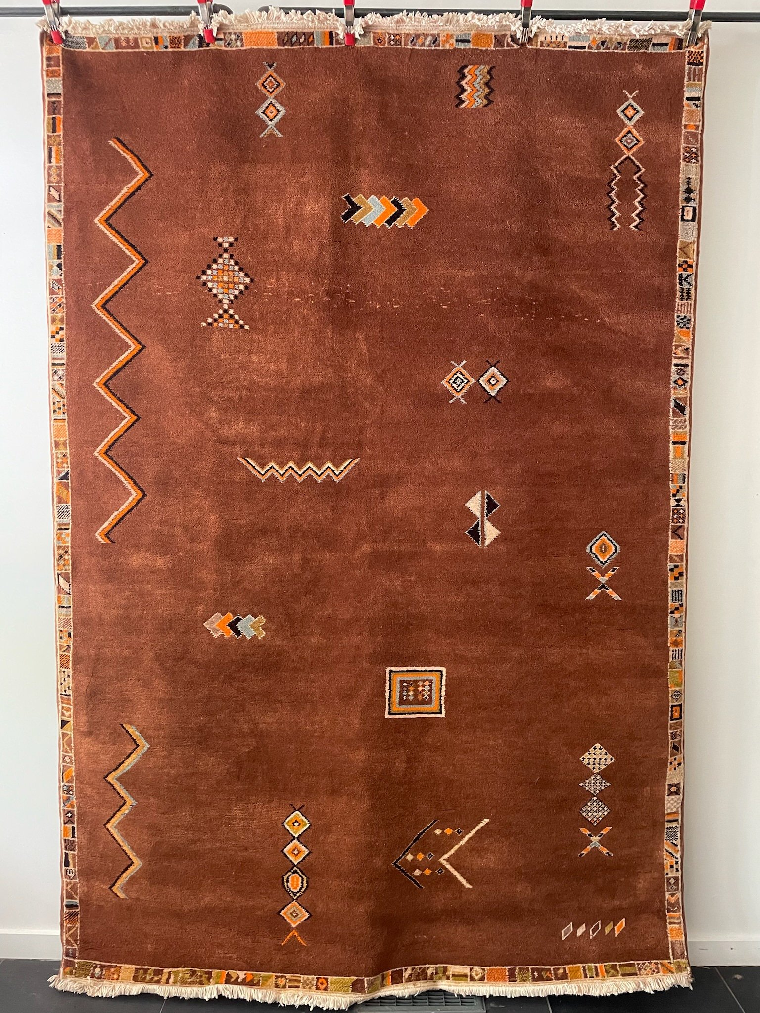 low pile, dense, hand-knotted moroccan wool rug with matte brown base and minimal multicolor berber motifs