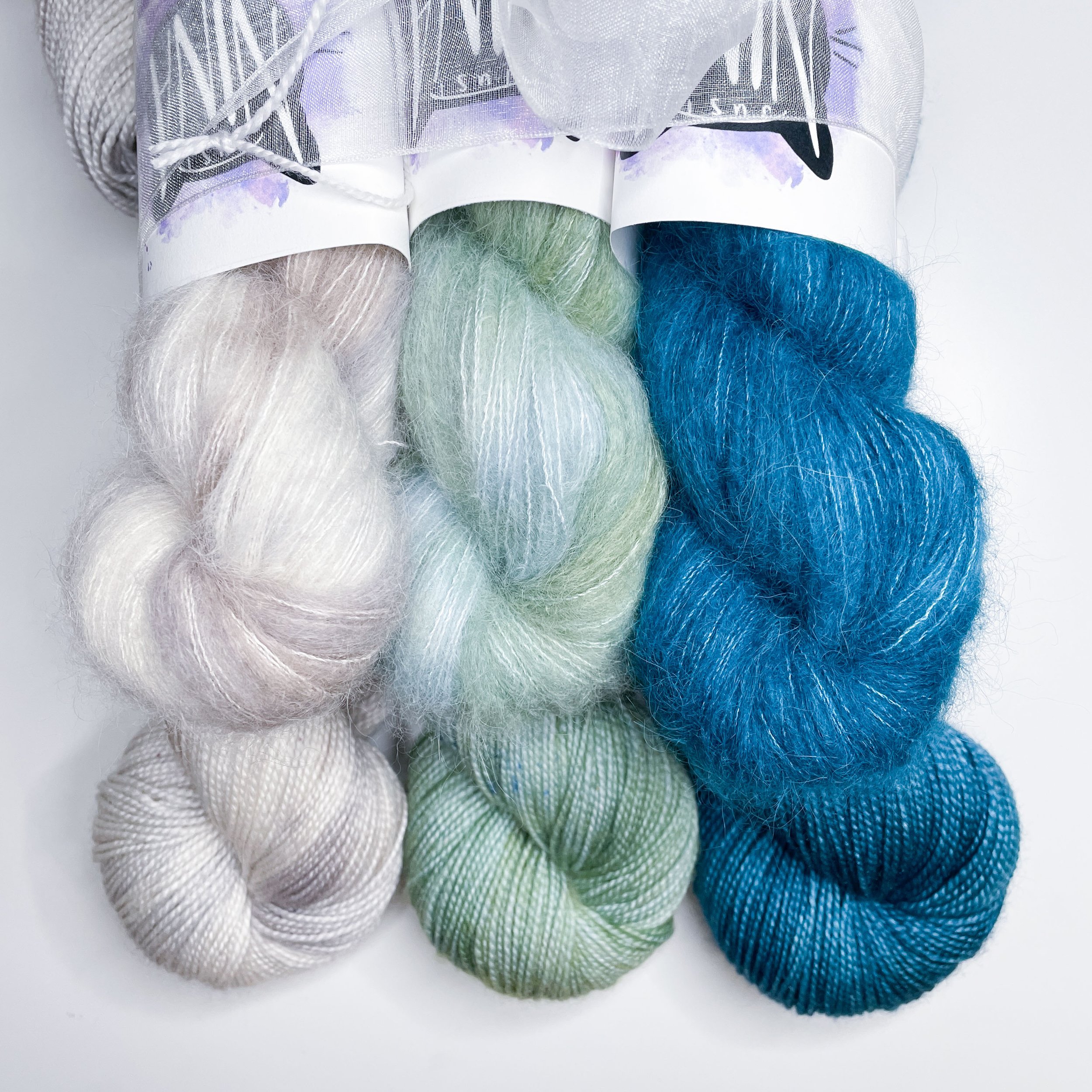 A bundle of six hanks of yarn (three in superwash wool and three in coordinating alpaca silk) hand dyed to create a fade from light warm grey to sage green to dark teal.