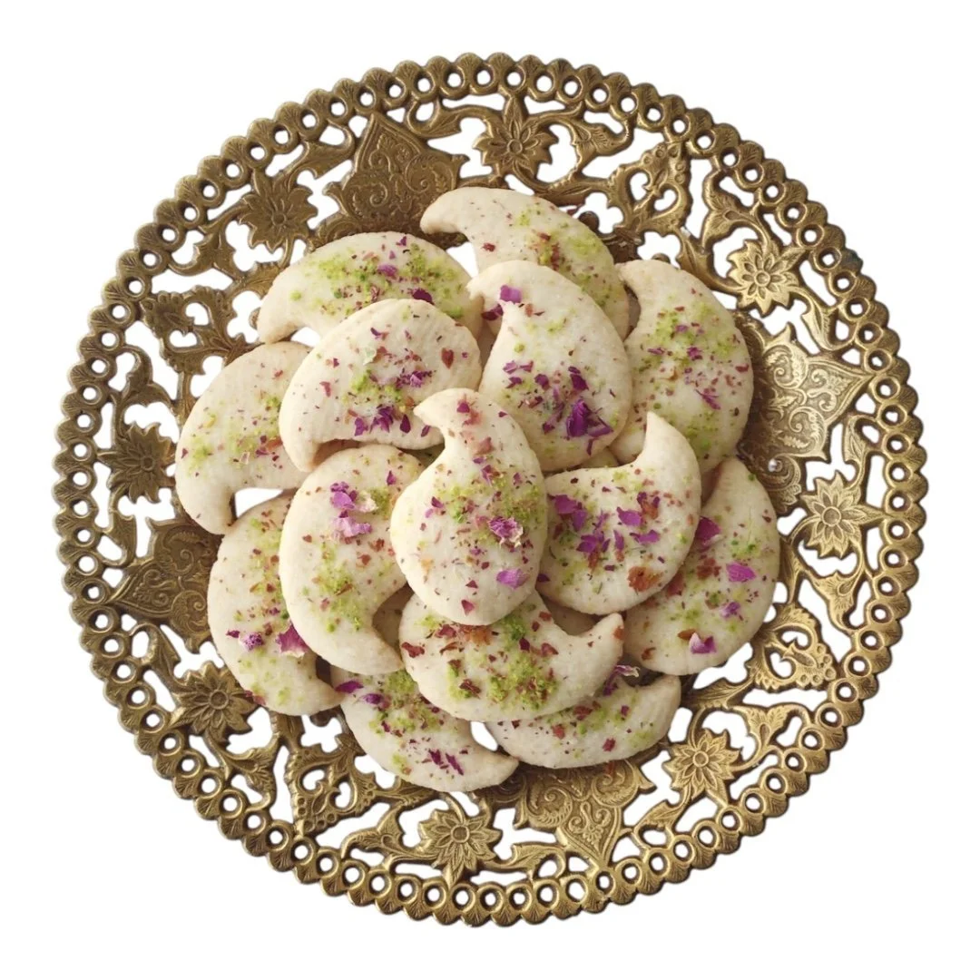 Plate of crescent-shaped cookies decorated with green and purple edible flower petals.