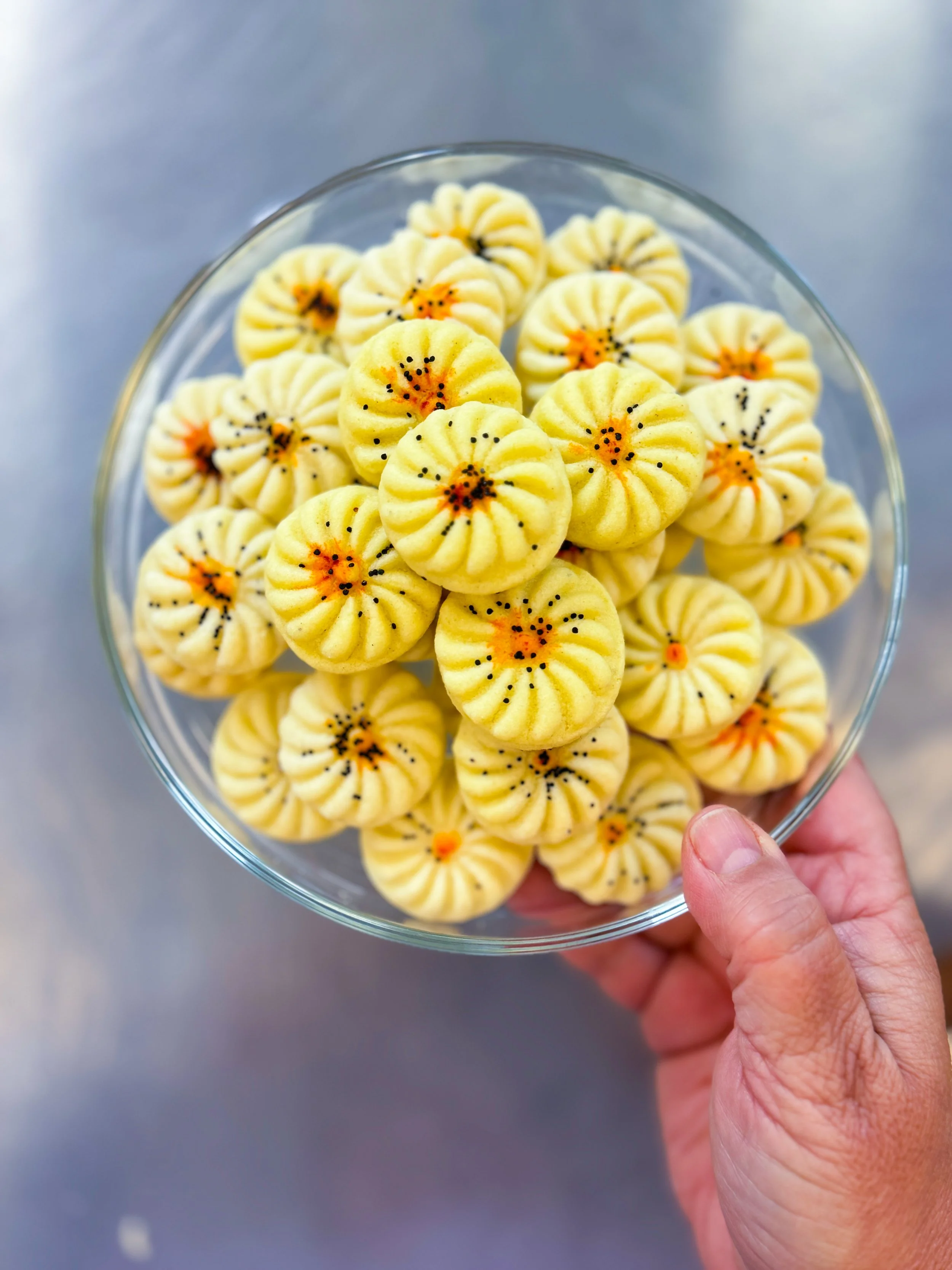 A hand holding a glass bowl filled with small yellow cookies decorated with orange and black sprinkles.