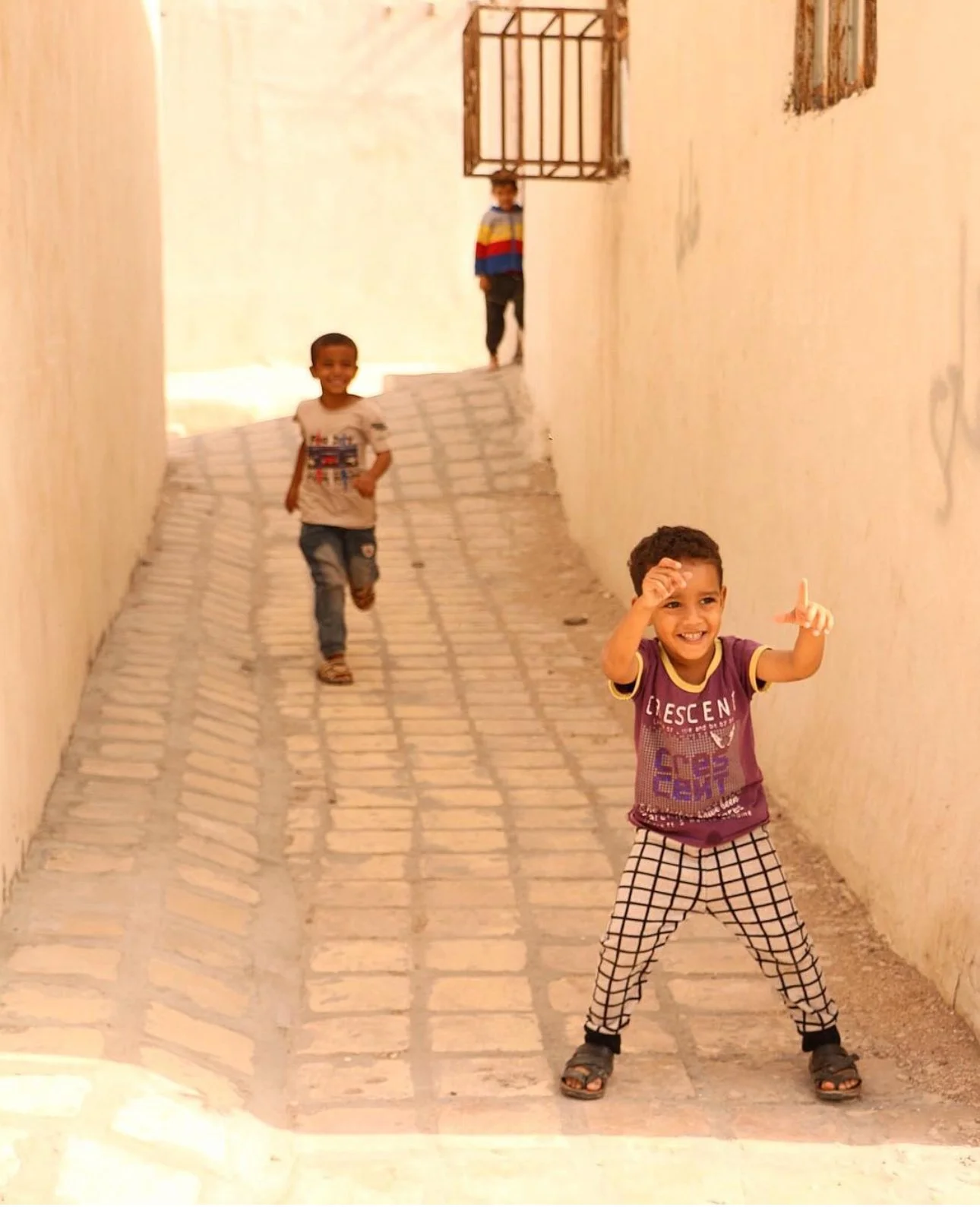 Three boys playing on a cobblestone alleyway with white walls, smiling and having fun.
