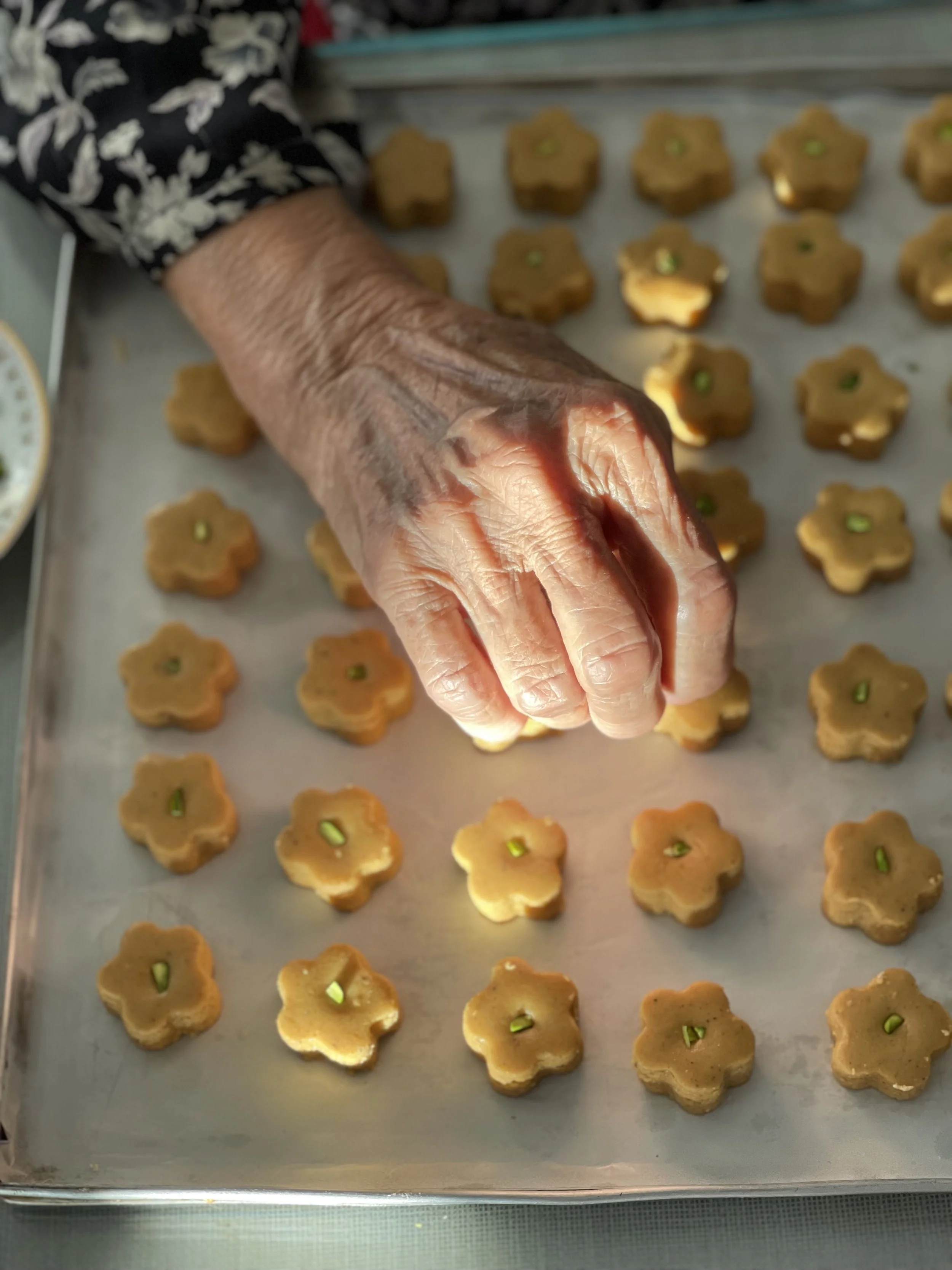 A close-up of a hand placing flower-shaped cookies with green filling on a baking tray lined with parchment paper.