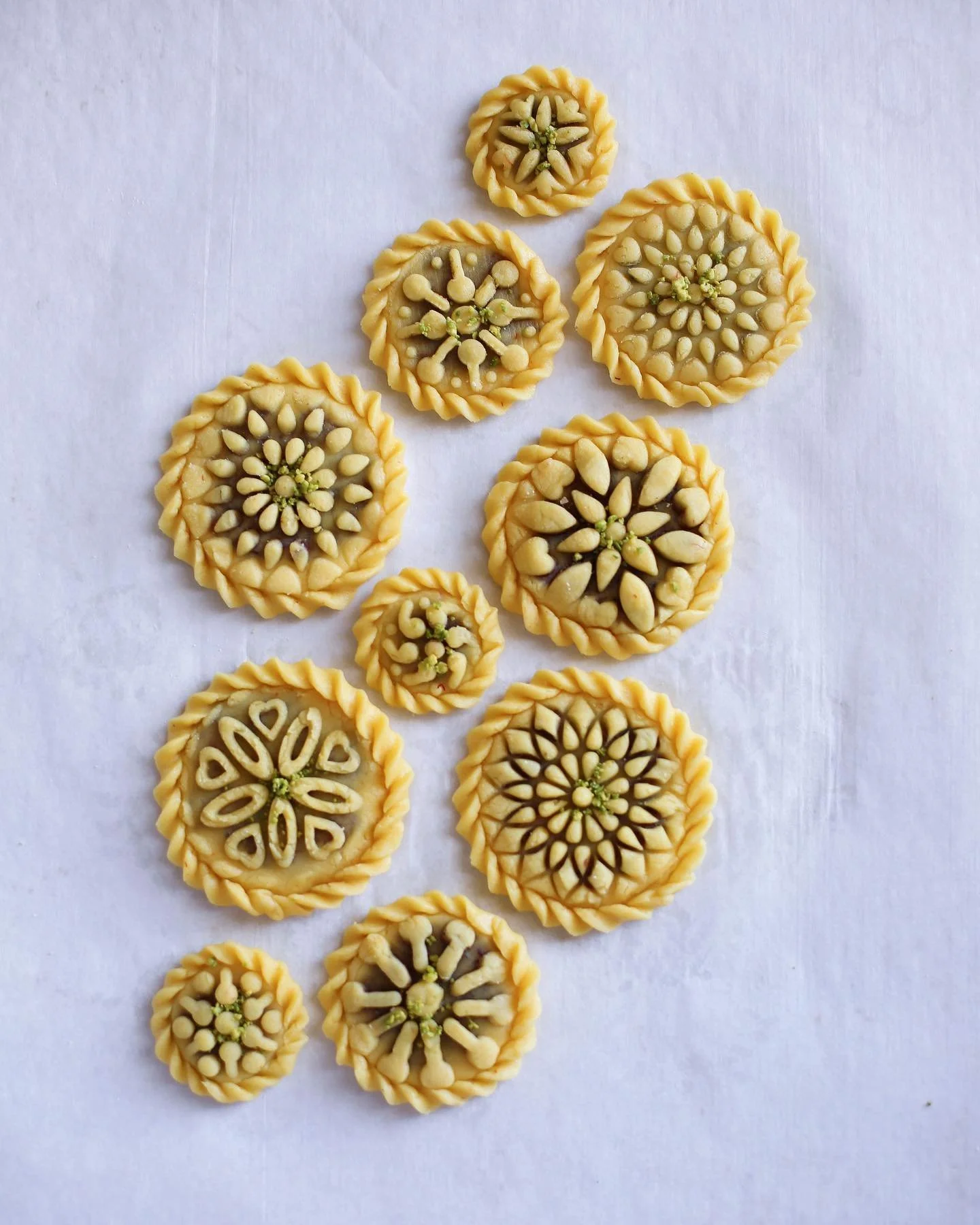 Assorted decorative cookies with intricate floral and geometric designs, topped with seeds or nuts, arranged on a white surface.
