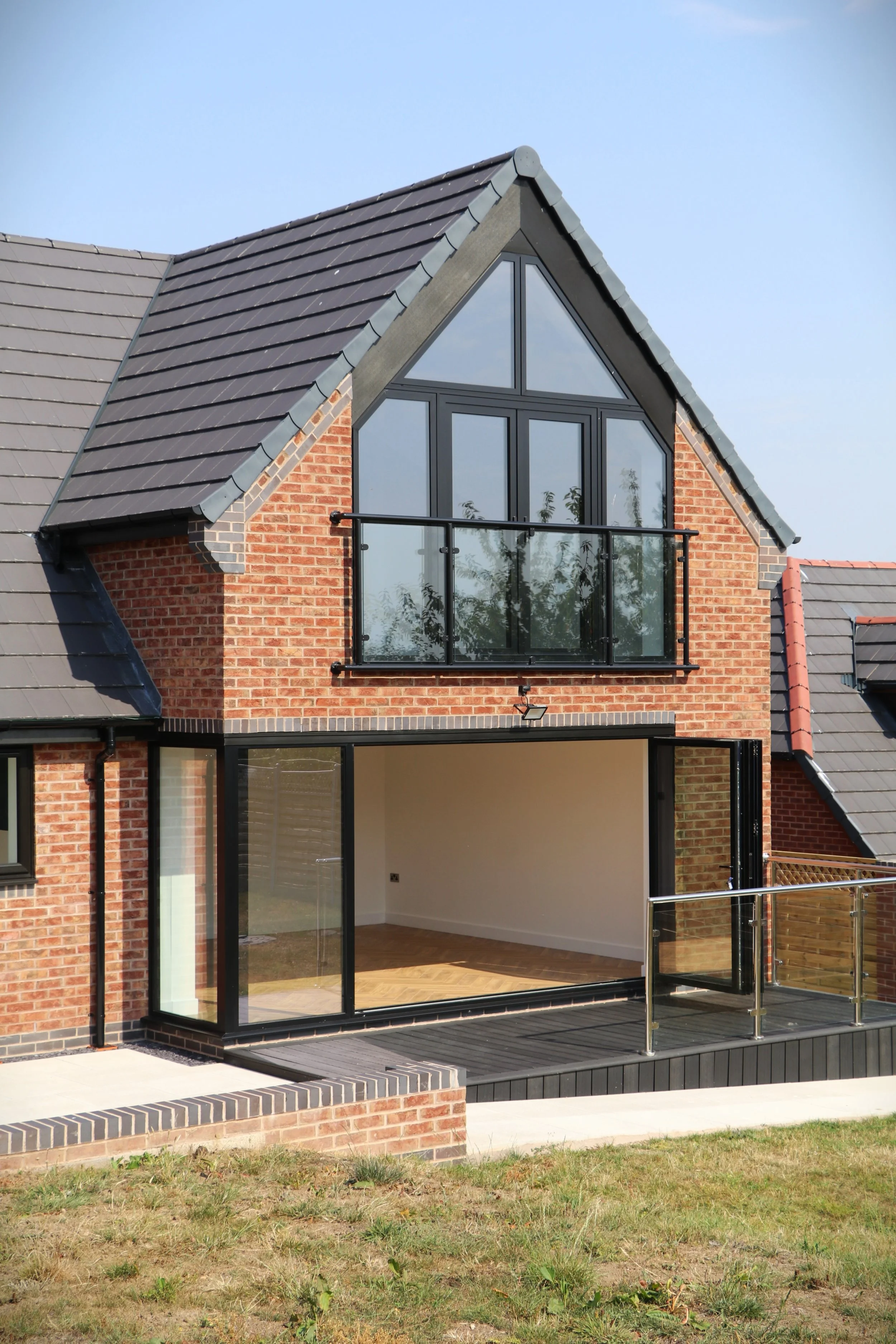  The rear elevation features an expansive first-floor glazed gable and Juliet balcony, alongside ground-floor corner bifold doors that take full advantage of the panoramic views. 