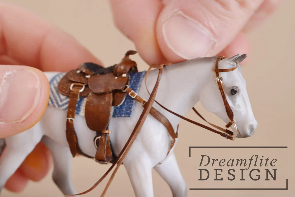 White human hands adjusting reins on a grey model horse with brown western saddle 