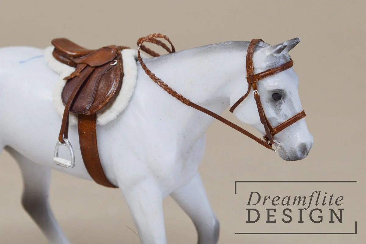  Grey model horse with a brown english saddle and brown bridle on a tan background 
