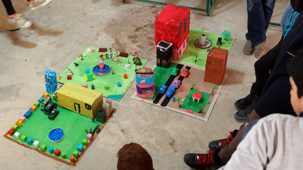 The completed "good" city with a school (guarded by soldiers), a park with children playing, homes with cars driving by, and a hospital tower with fountain in front. 