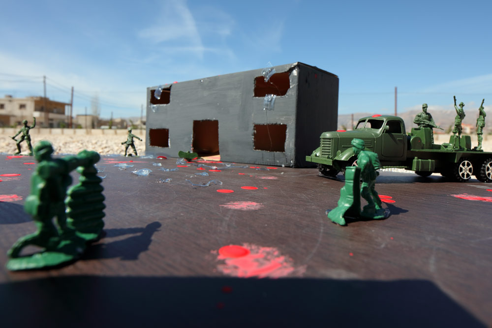 The blown up shell of a school, now at the center of a fight between soldiers. Blood spatters the ground in-between. 