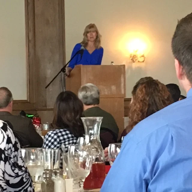 Jane Grote Abell of Donatos at the podium and the shoulder of a man in a blue shirt in the foreground.