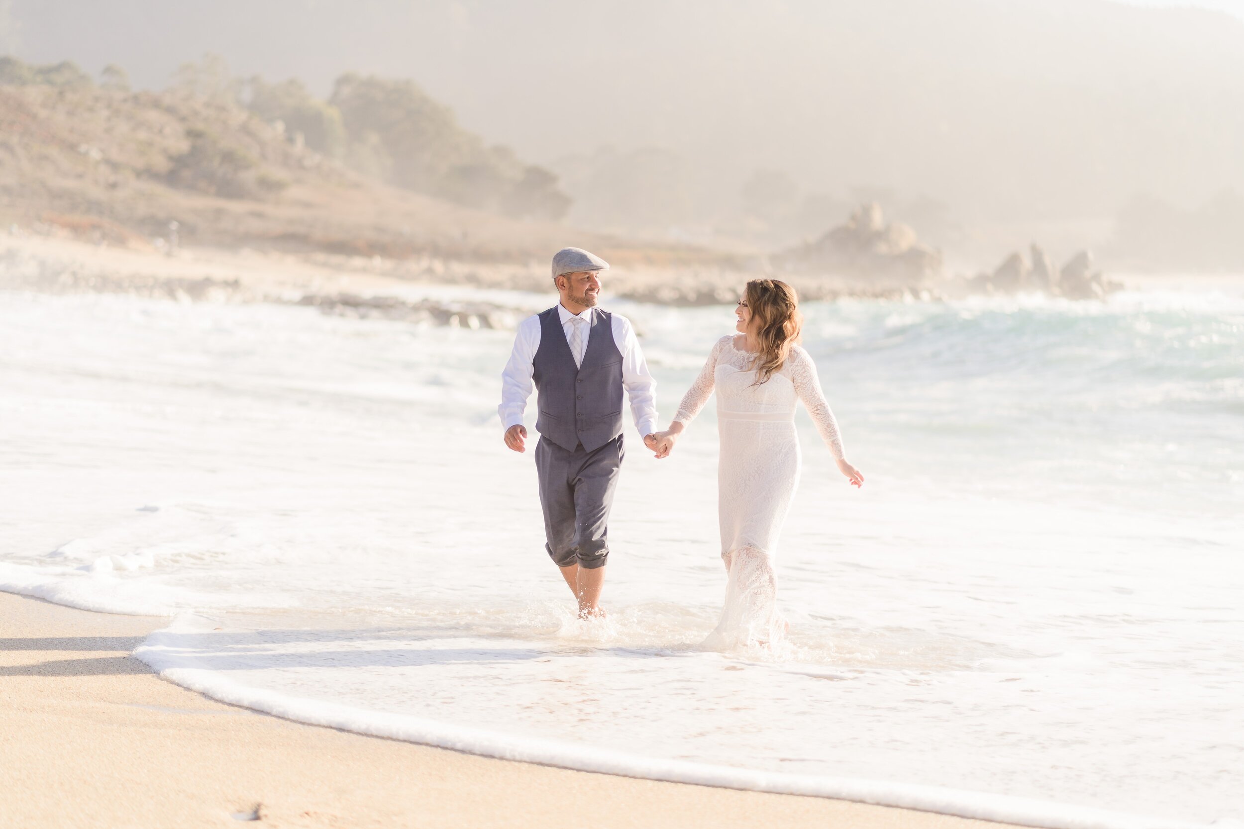 bride and groom walking in the ocean water at carmel beach in carmel ca