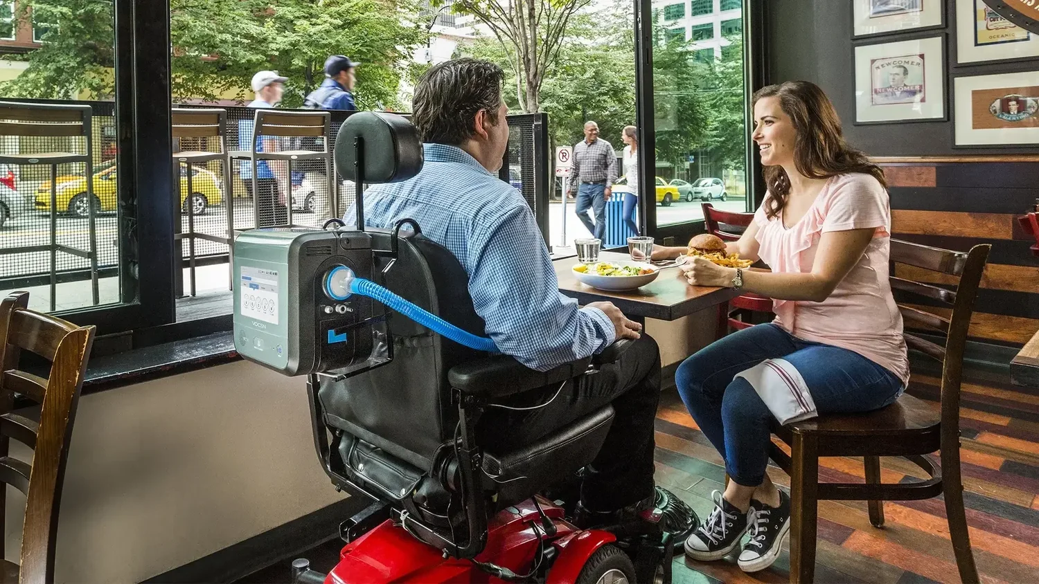 Patient using a VOCSN ventilator mounted on a power wheelchair at a restaurant