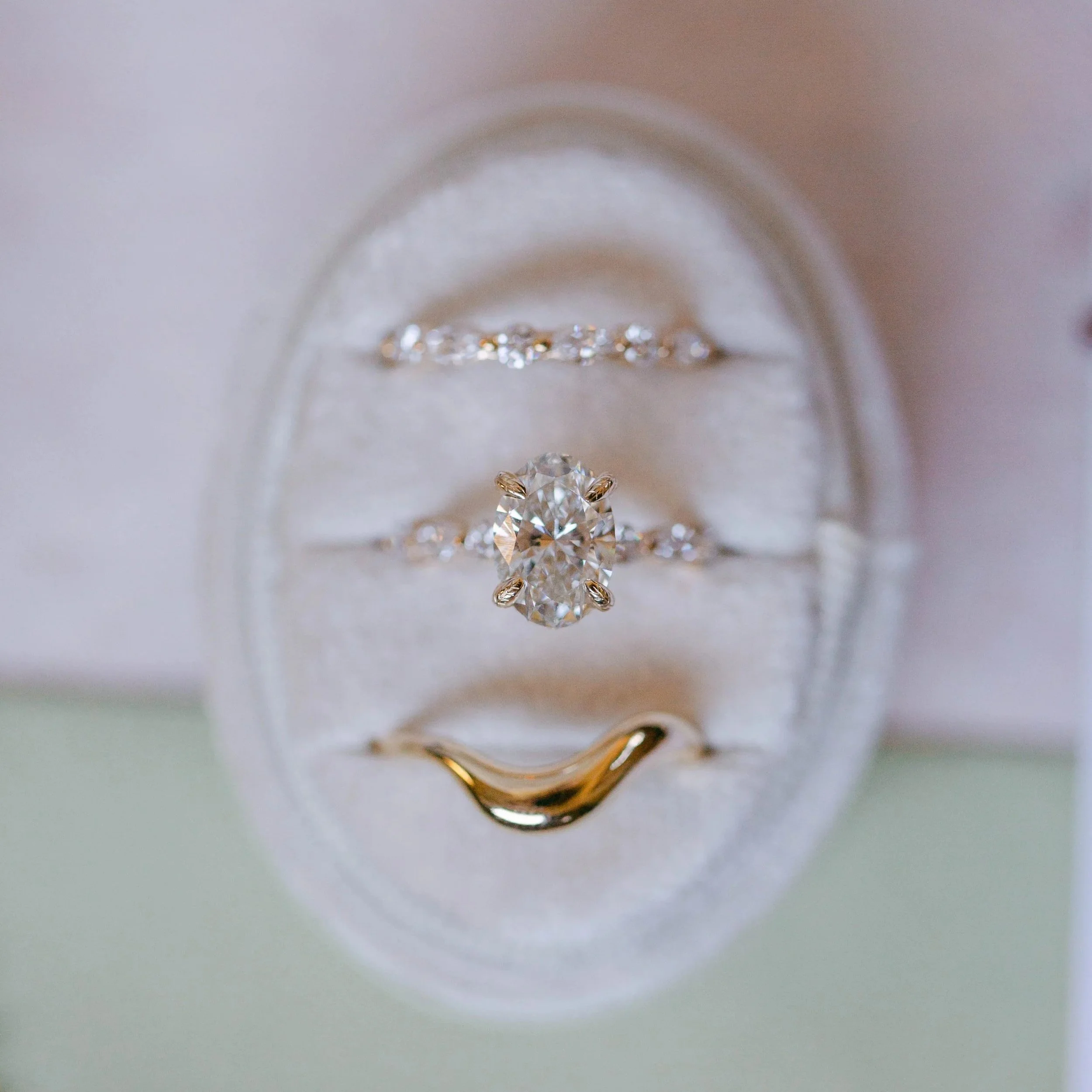 Close-up of a custom made Lady Cromer Jewelry diamond engagement ring in a white velvet ring box, with custom made wedding bands on either side, all reflecting light beautifully and showcasing the sparkle of the diamonds. Photo by Adriana Michele