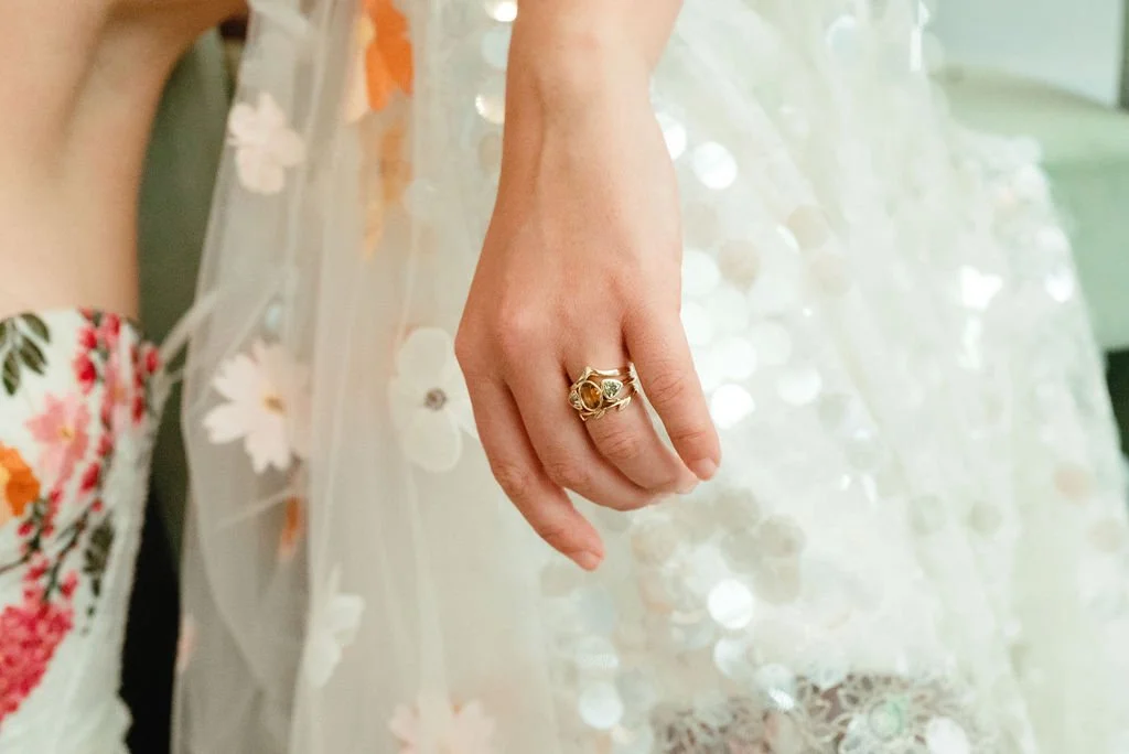 Close-up of a woman's hand with a gold ring, resting on a floral and sequin-adorned gown.