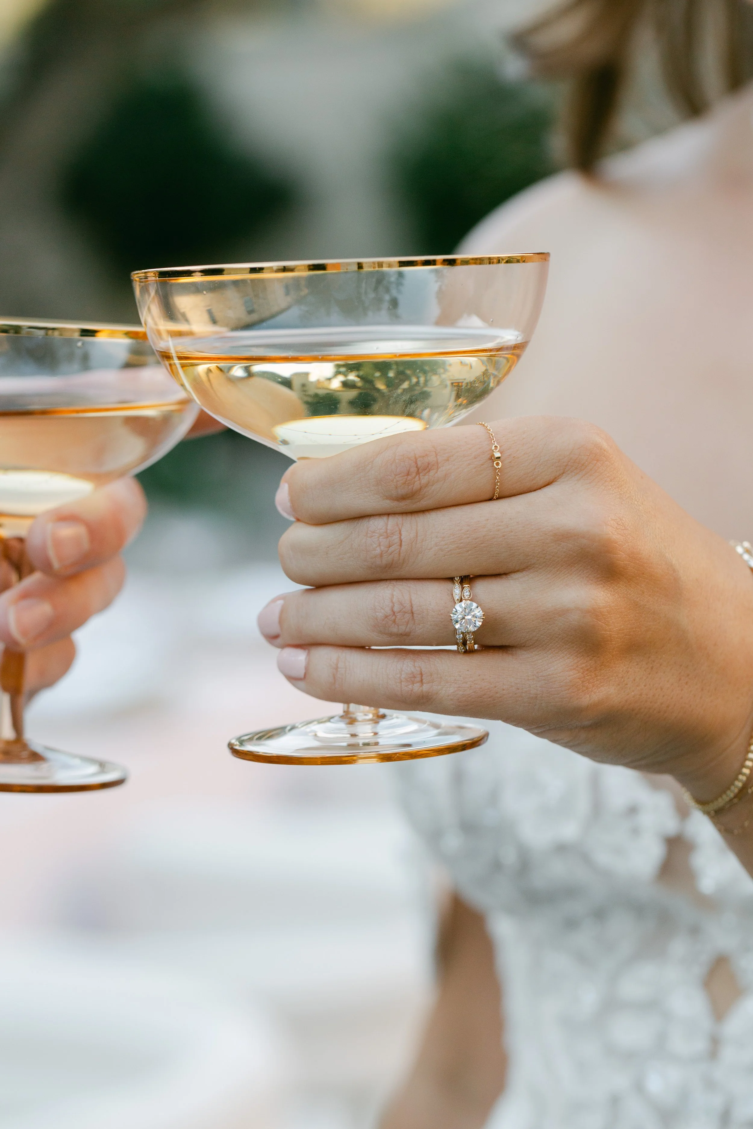 Bride holding a champagne glass with custom 14k gold and diamond engagement ring and a gold bracelet.  Photography by Adriana Michele Photography