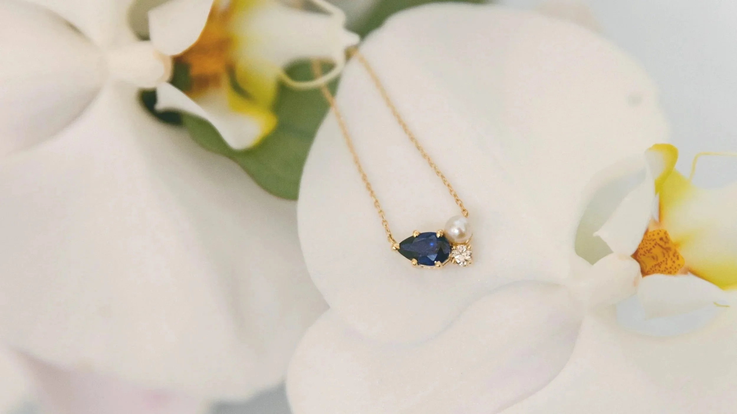 A unique cluster style necklace in 14k gold with a sapphire, diamond, and pearl which was custom designed and made by Lady Cromer Jewelry.