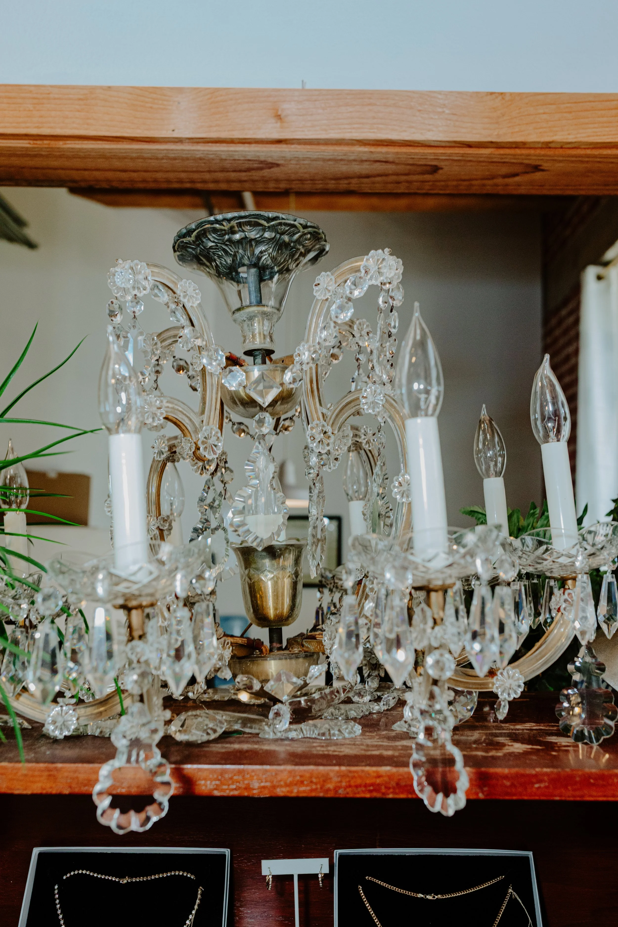 Close-up of a vintage crystal chandelier in the Lady Cromer Jewelry showroom, adorned with hanging decorative crystals, set above a wooden surface with jewelry displays below. 