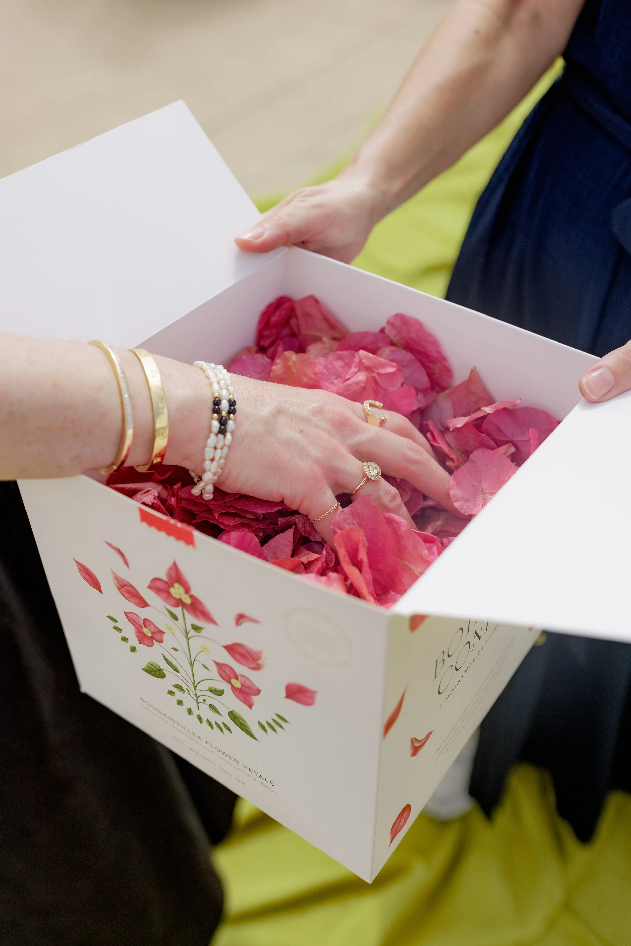 Hands holding a white flower petal gift box with pink flower petals inside. Sapphire and diamond custom made ring and custom jewelry made to order in San Diego. 