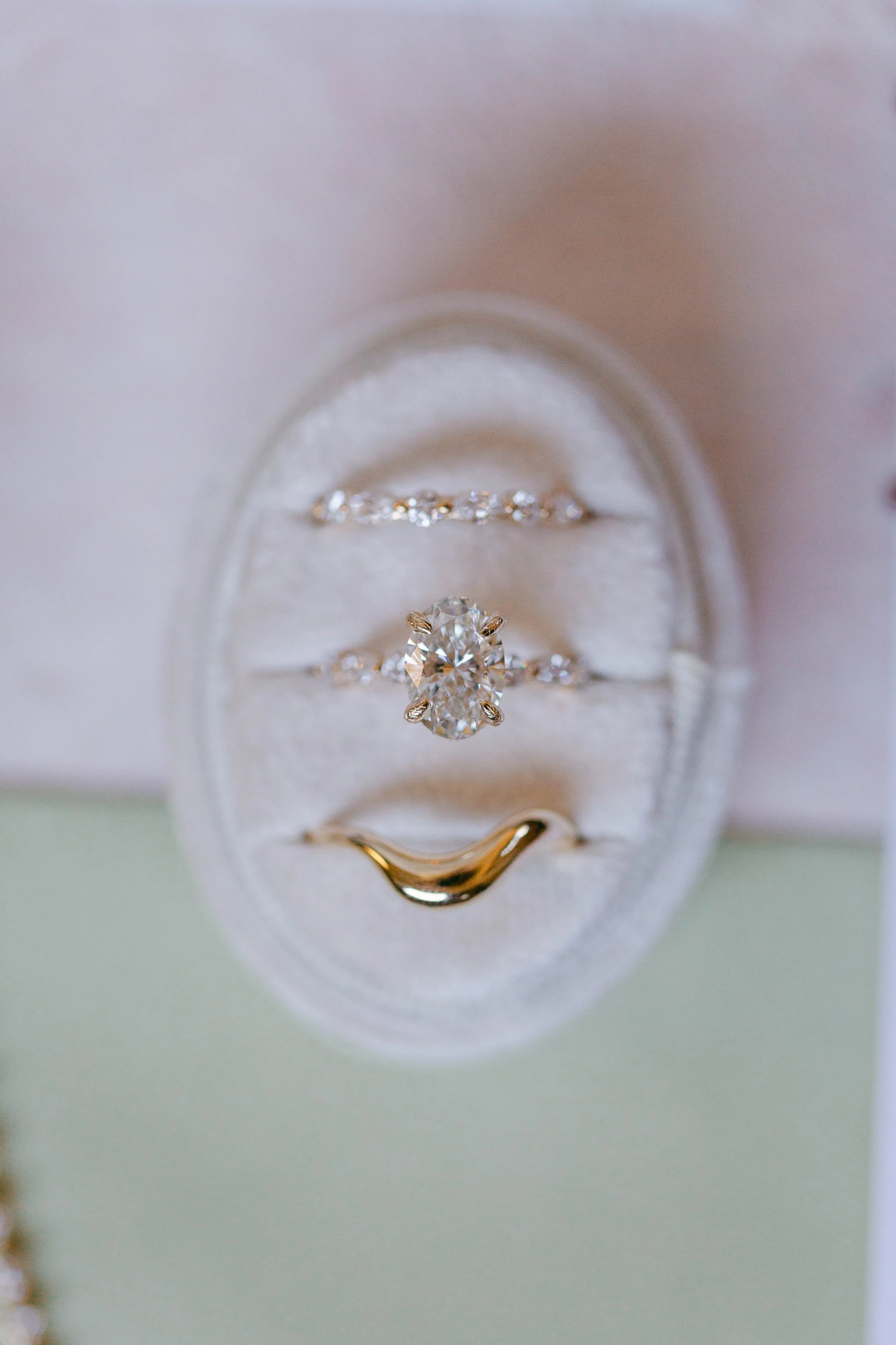 Close-up of a custom made Lady Cromer Jewelry diamond engagement ring in a white velvet ring box, with custom made wedding bands on either side, all reflecting light beautifully and showcasing the sparkle of the diamonds. Photo by Adriana Michele