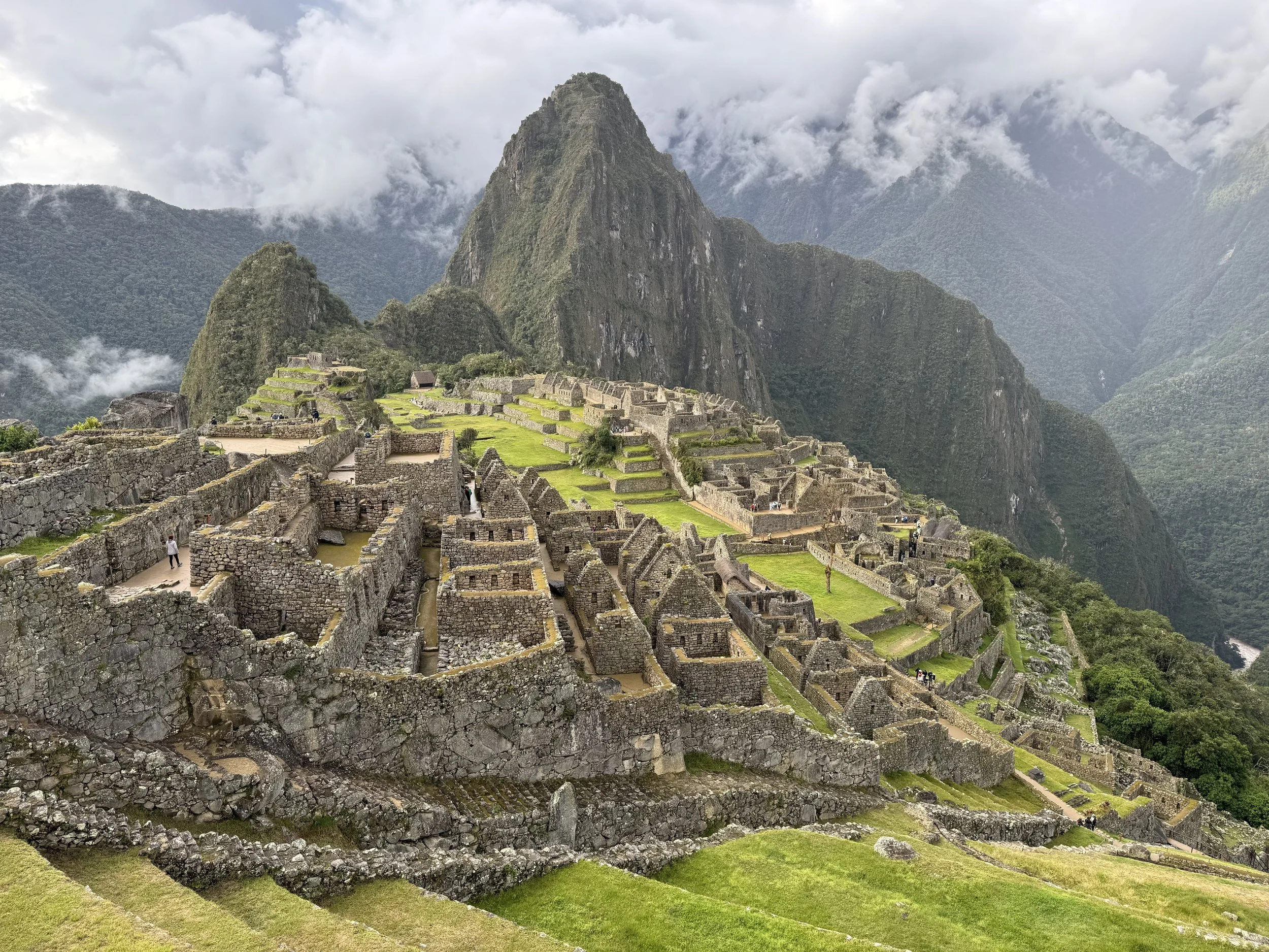 Ancient Inca ruins at Machu Picchu nestled in green mountains with clouds in the sky.