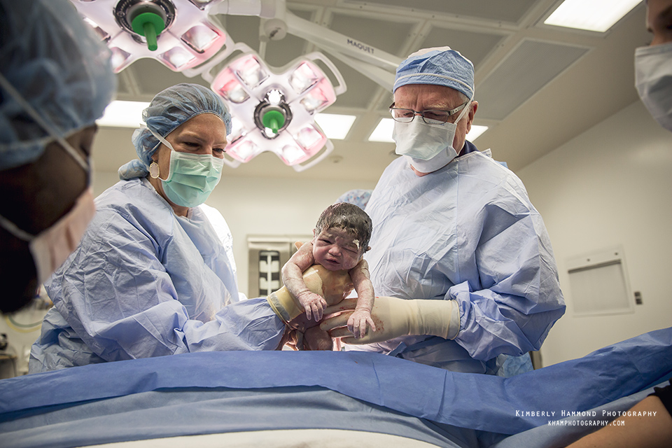 Doctors hold up new baby for parents to see during family centered cesarean in Fort Worth, TX.