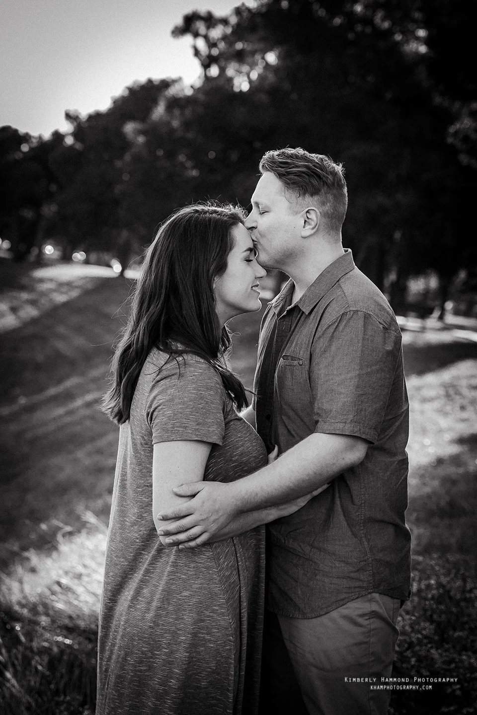 Man kisses fiance on forehead during their engagement photography session at Trinity Park in Fort Worth, TX.