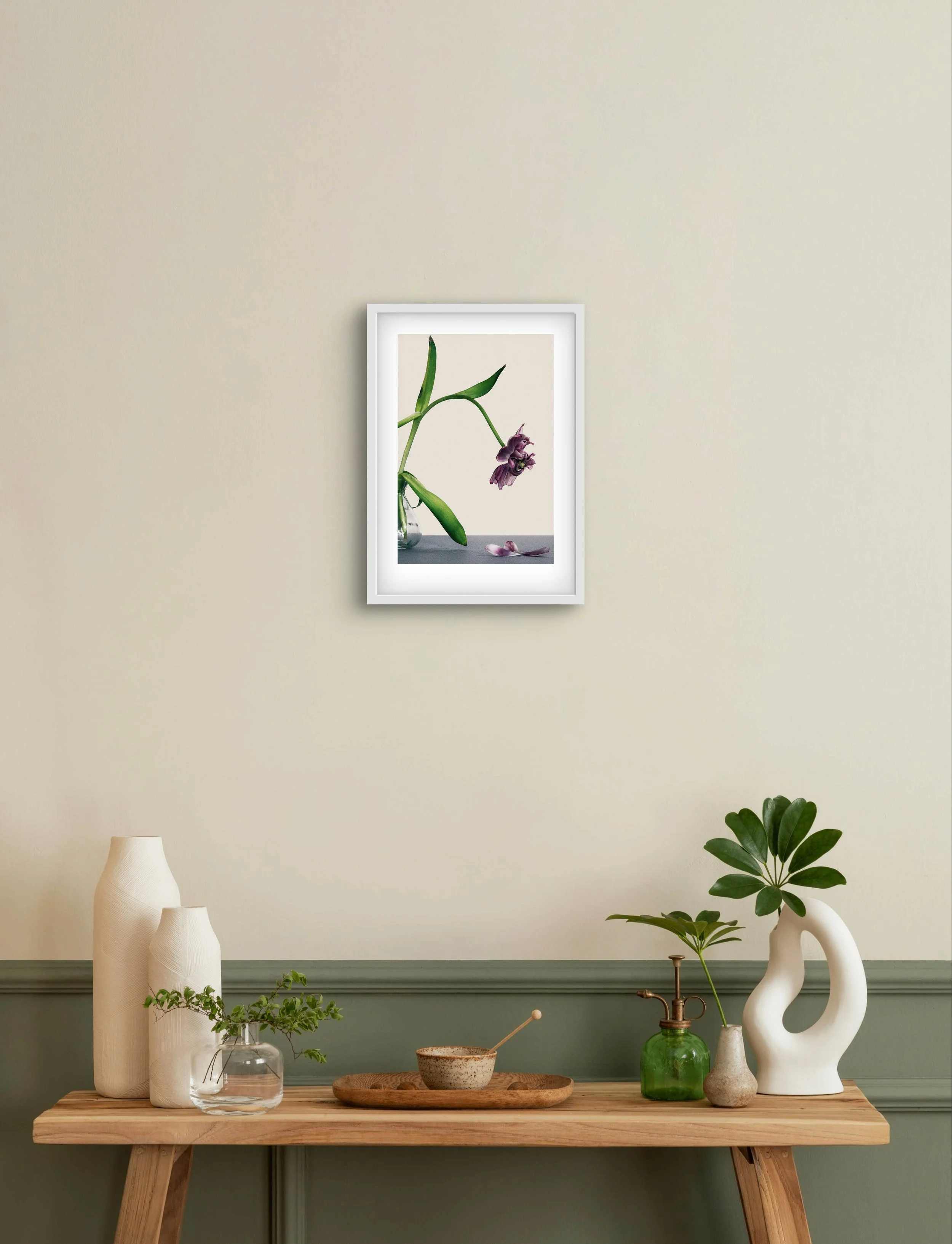 Framed print of a fading tulip with fallen petals, displayed on a neutral wall in a quiet interior. The image adds a sense of stillness and transience to the space.