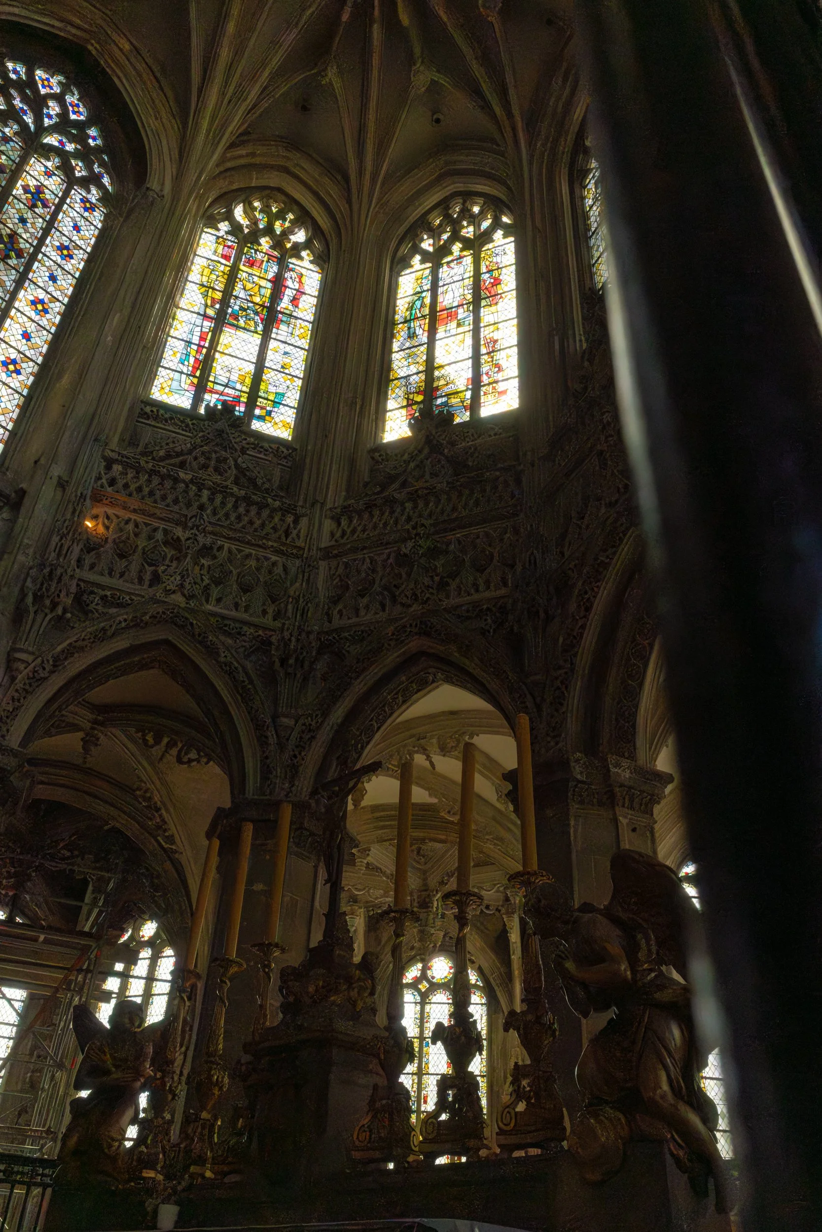 Interior view of a Gothic-style church or cathedral with stained glass windows and ornate architecture, featuring multiple sculptures and decorative elements.