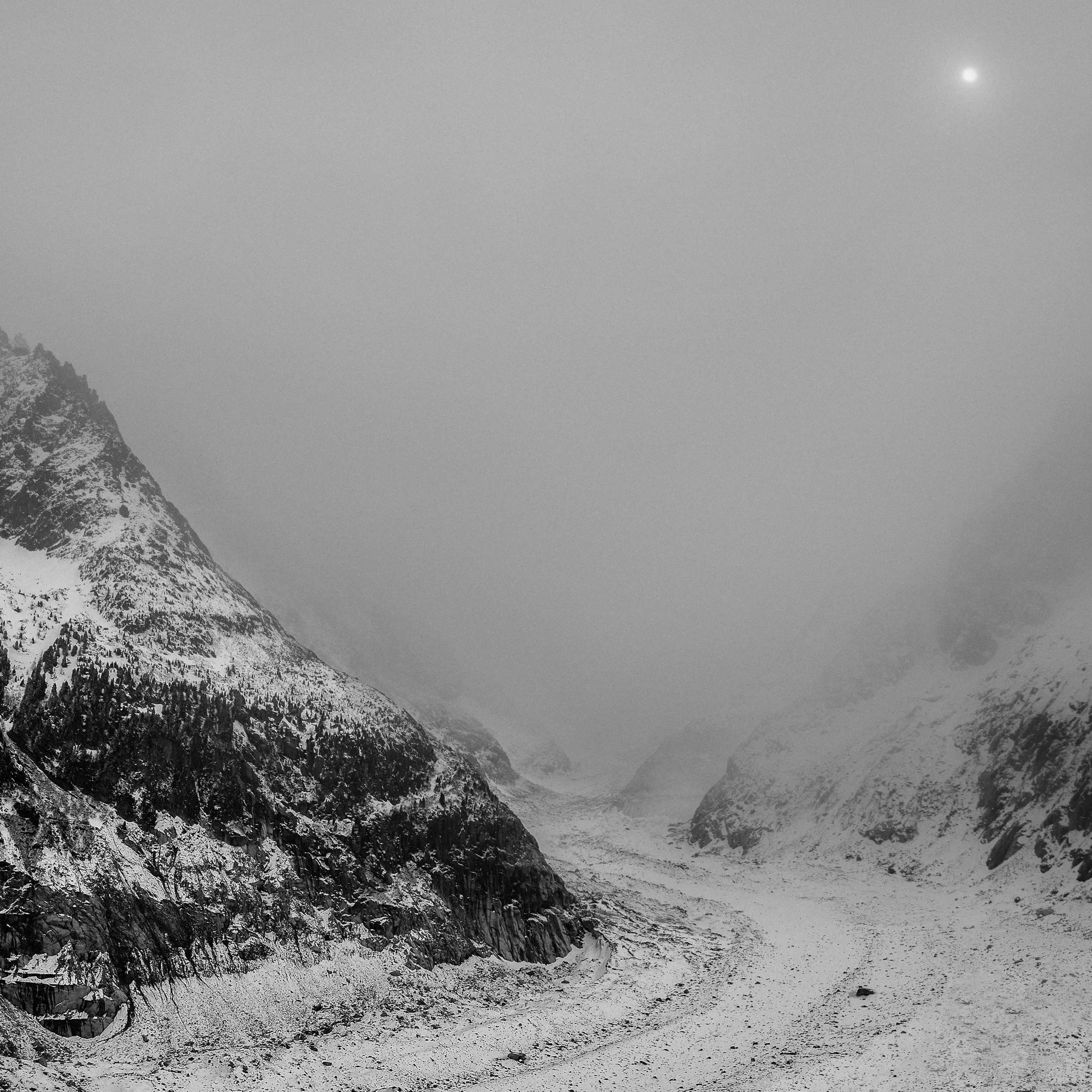 Snow-capped mountains in a rugged landscape with a cloudy sky and a visible moon.