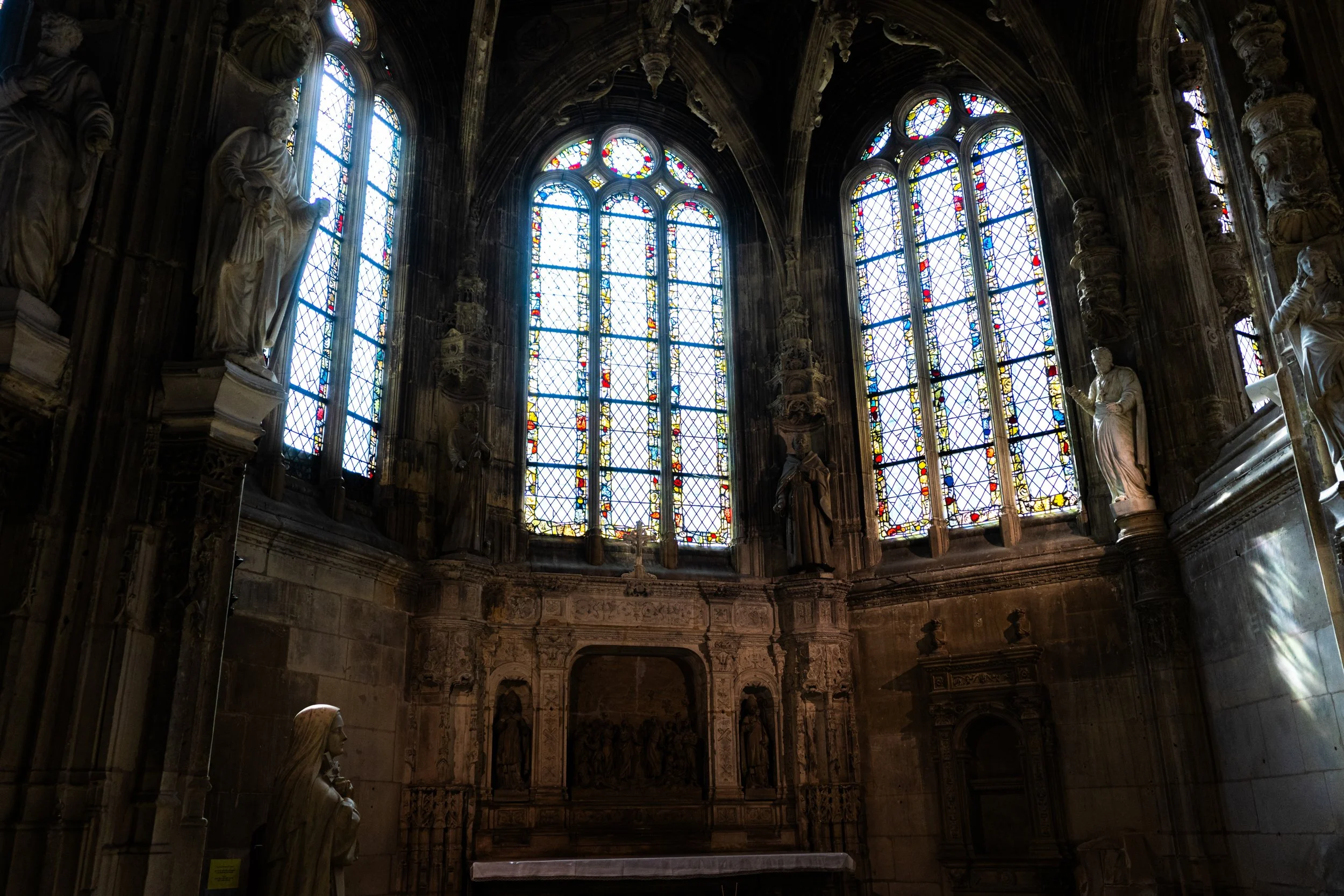 Inside view of a cathedral with large stained glass windows and ornate stone sculptures.