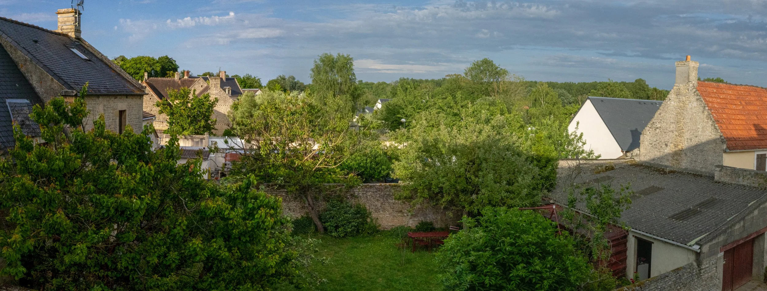 A view of a small European town with stone houses, lush green trees, and a cloudy sky.