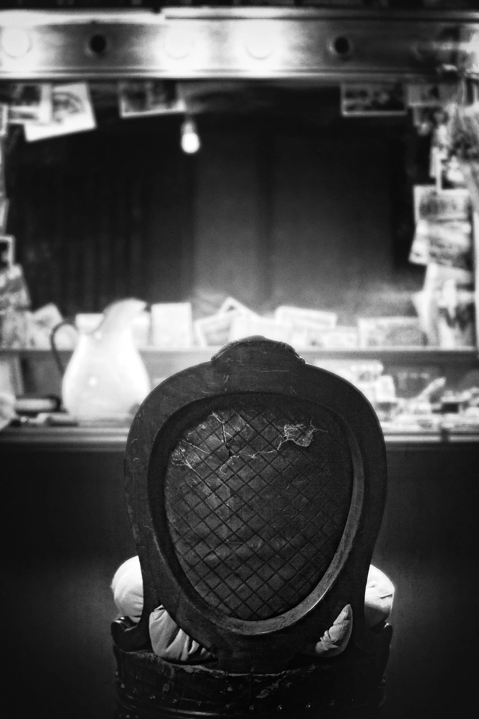 A child sitting in a chair with their back towards the camera, holding a tennis racket. The background appears to be a wood-paneled room with shelves and photographs.