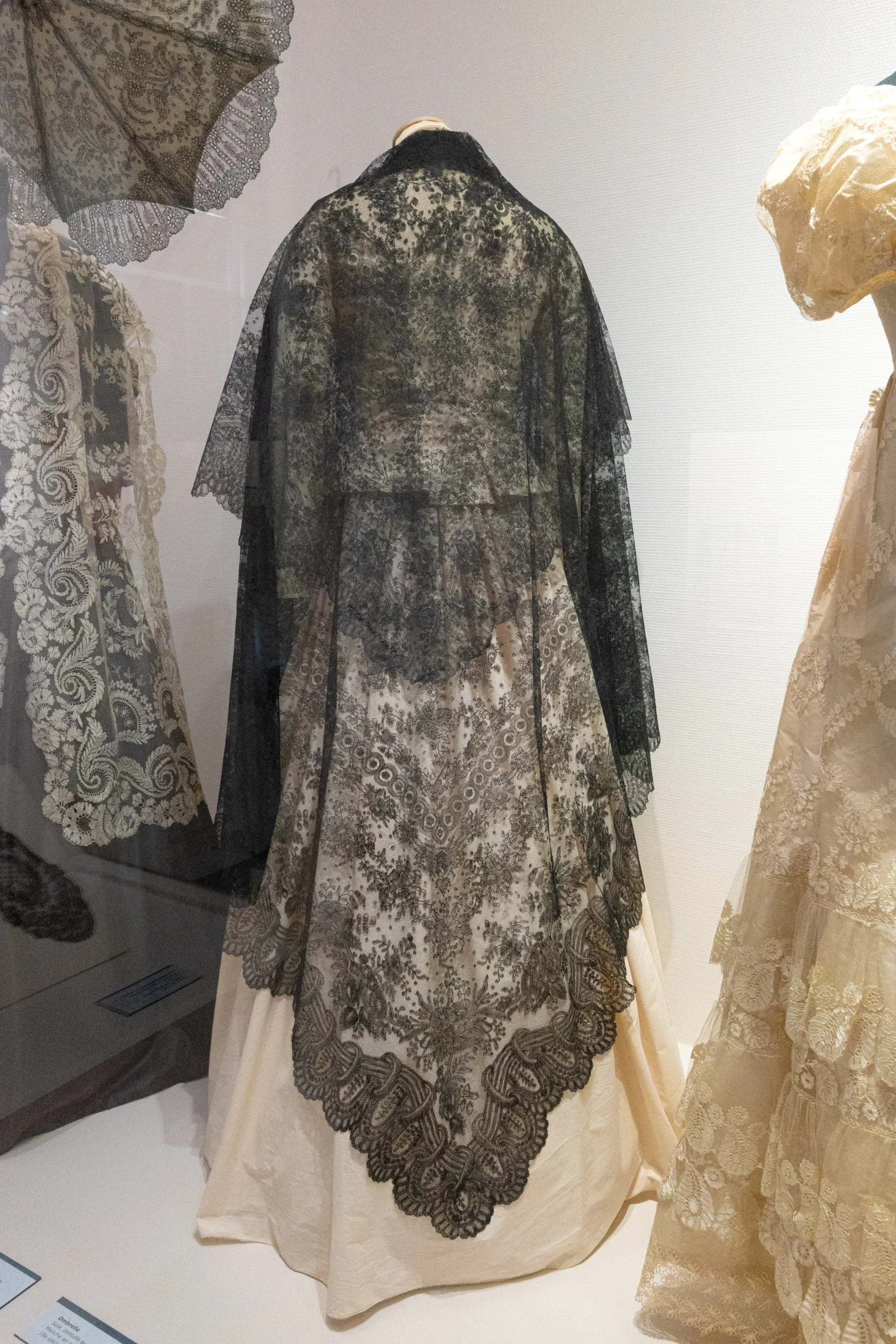 Display of vintage lace and embroidered skirts and dresses in an exhibition, featuring detailed black and cream lace patterns.