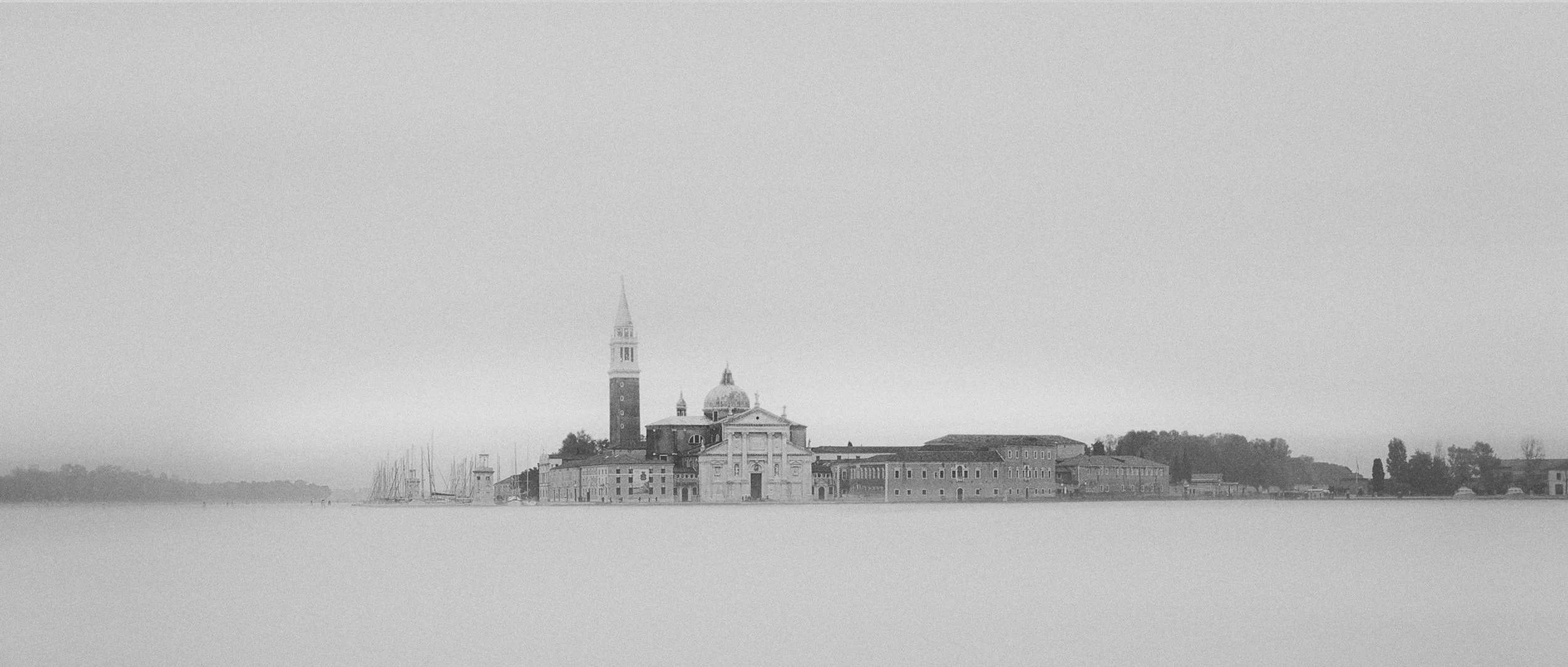 Black and white photo of a historic island with a church, bell tower, and other buildings, surrounded by water
