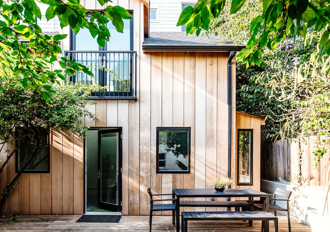 cottage facade with wood paneling and black trim windows and doors and black sitting area.jpg