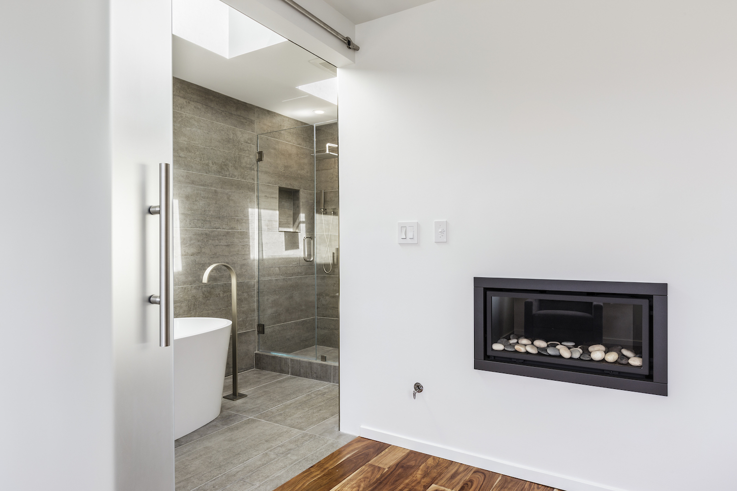 bathroom with fireplace and white tub and brushed nickel fixtures and grey tile and glass doors.jpg