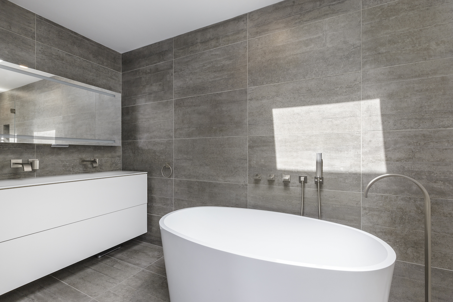 bathroom with grey tile and white vanity and white tub and brushed nickel fixtures.jpg