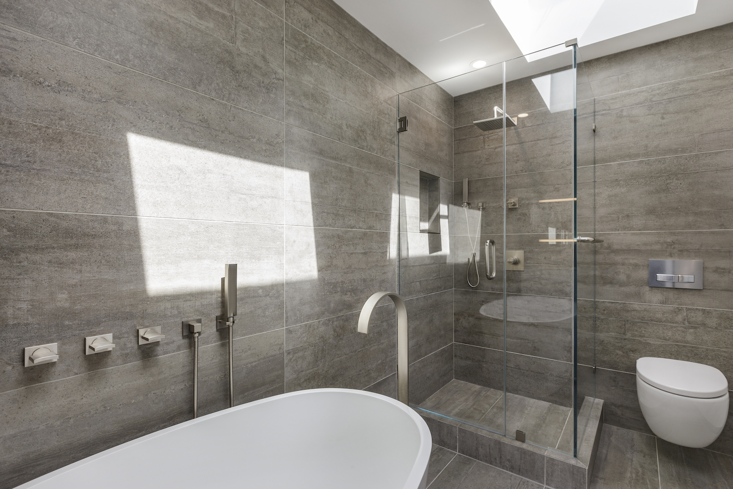 bathroom with grey wall tile and stall shower and soaking tub and wall mounted toilet and brushed nickel fixtures.jpg