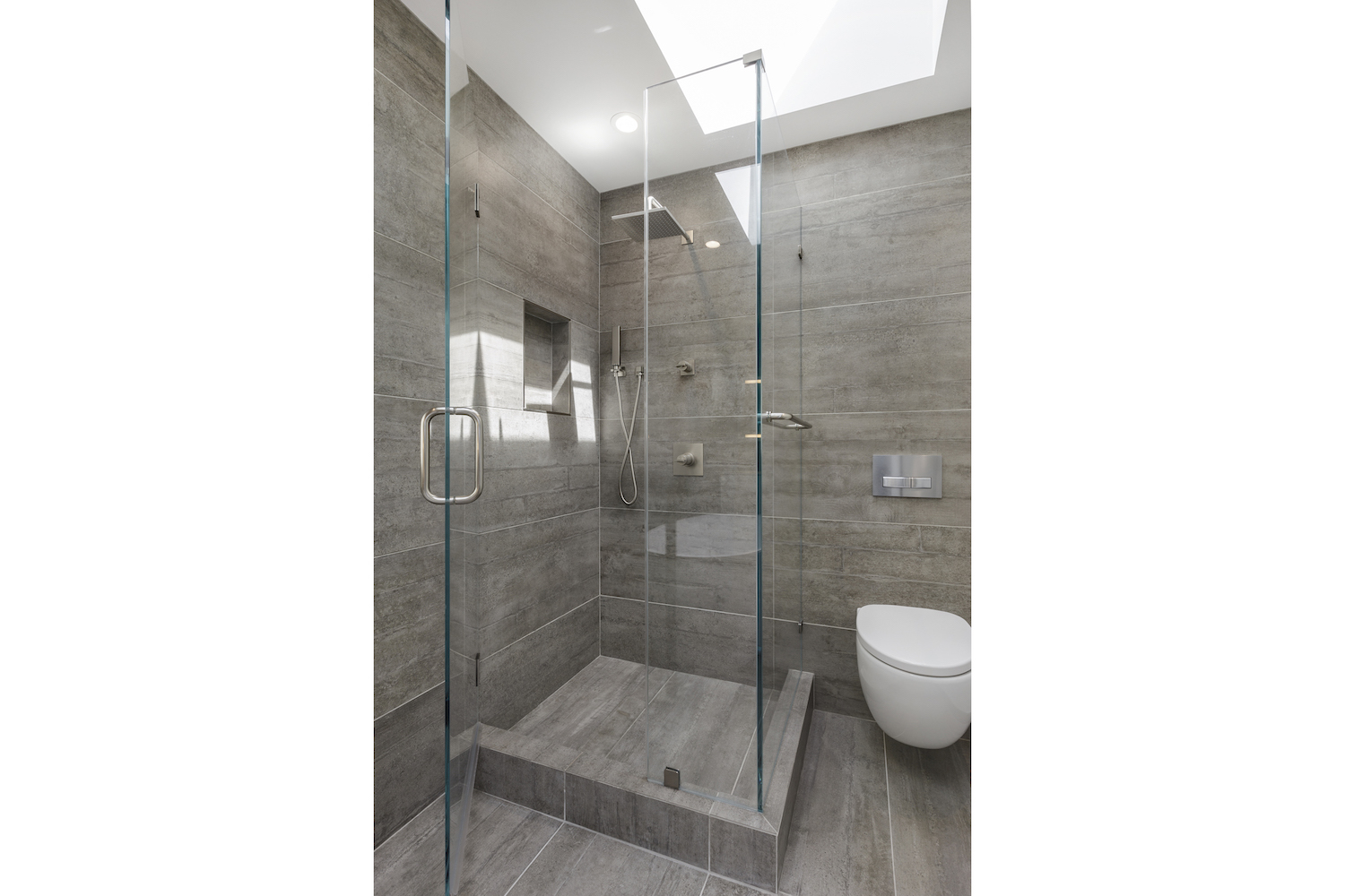 bathroom with stall shower with grey tile and stainless steel fixtures and glass walls.jpg
